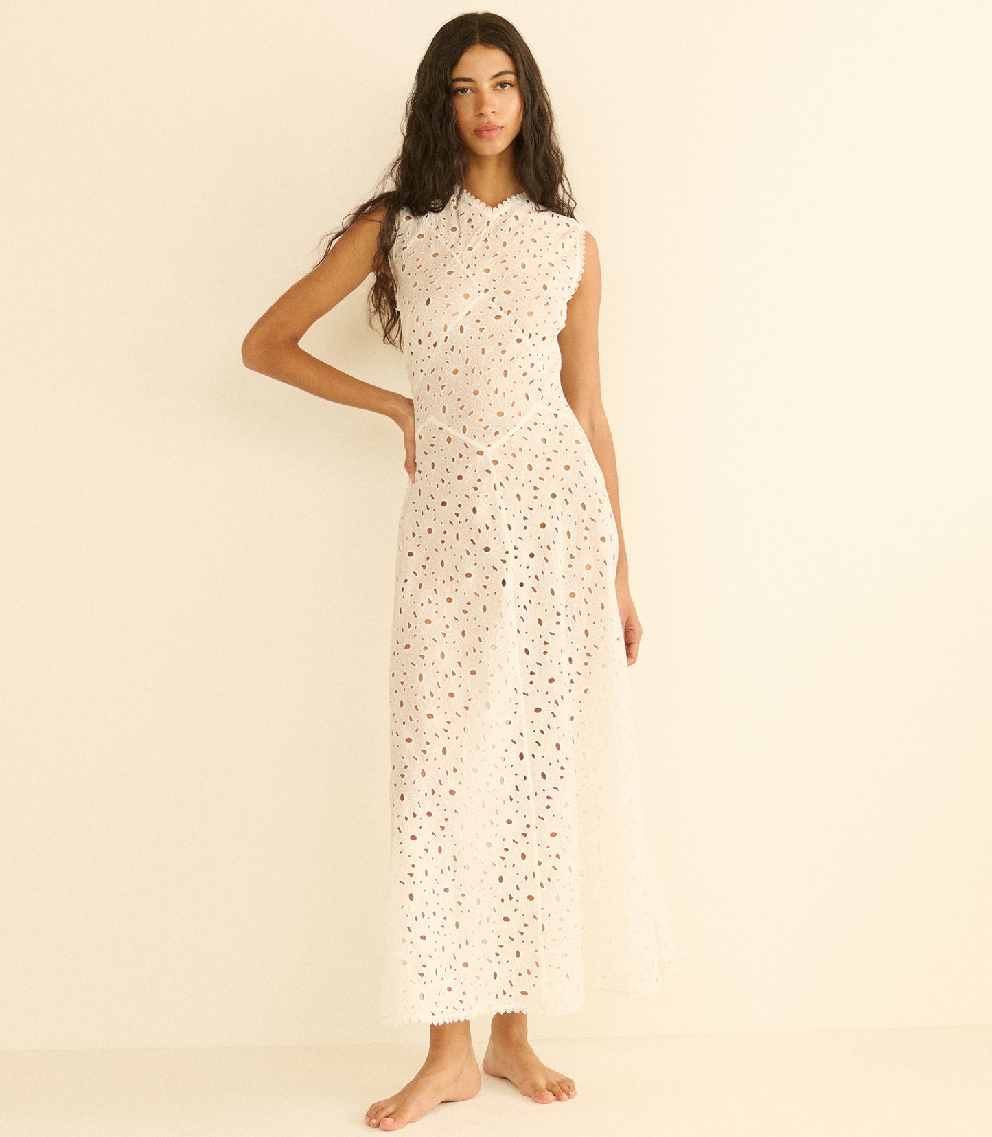 Woman wearing a long, white dress with a subtle pattern on a beige background