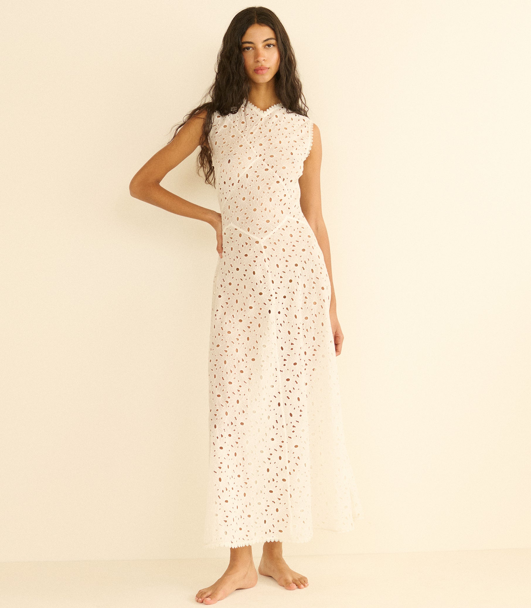 Woman wearing a long, white dress with a subtle pattern on a beige background