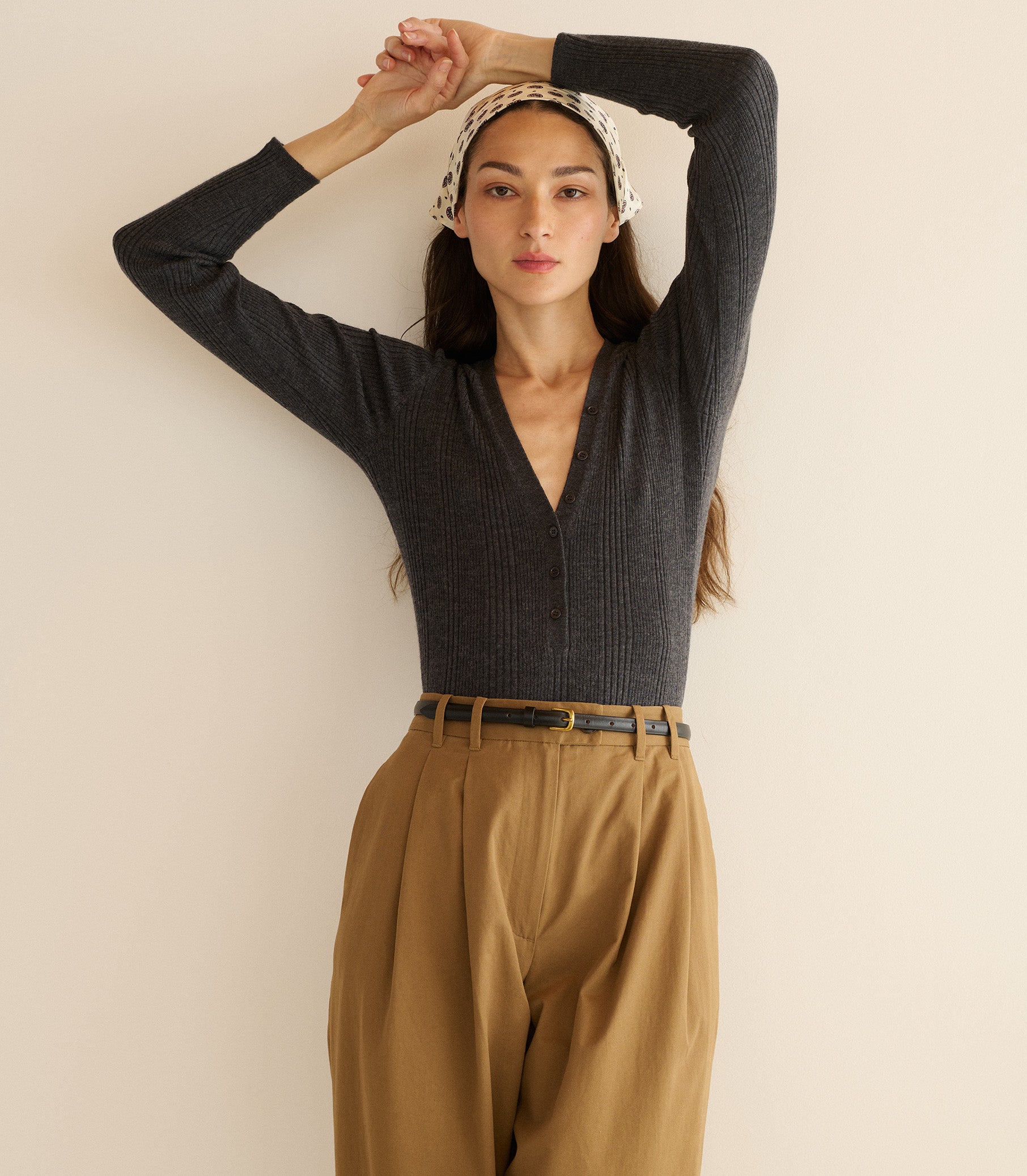 Woman wearing a dark gray long-sleeve top and tan pants against a beige background 1
