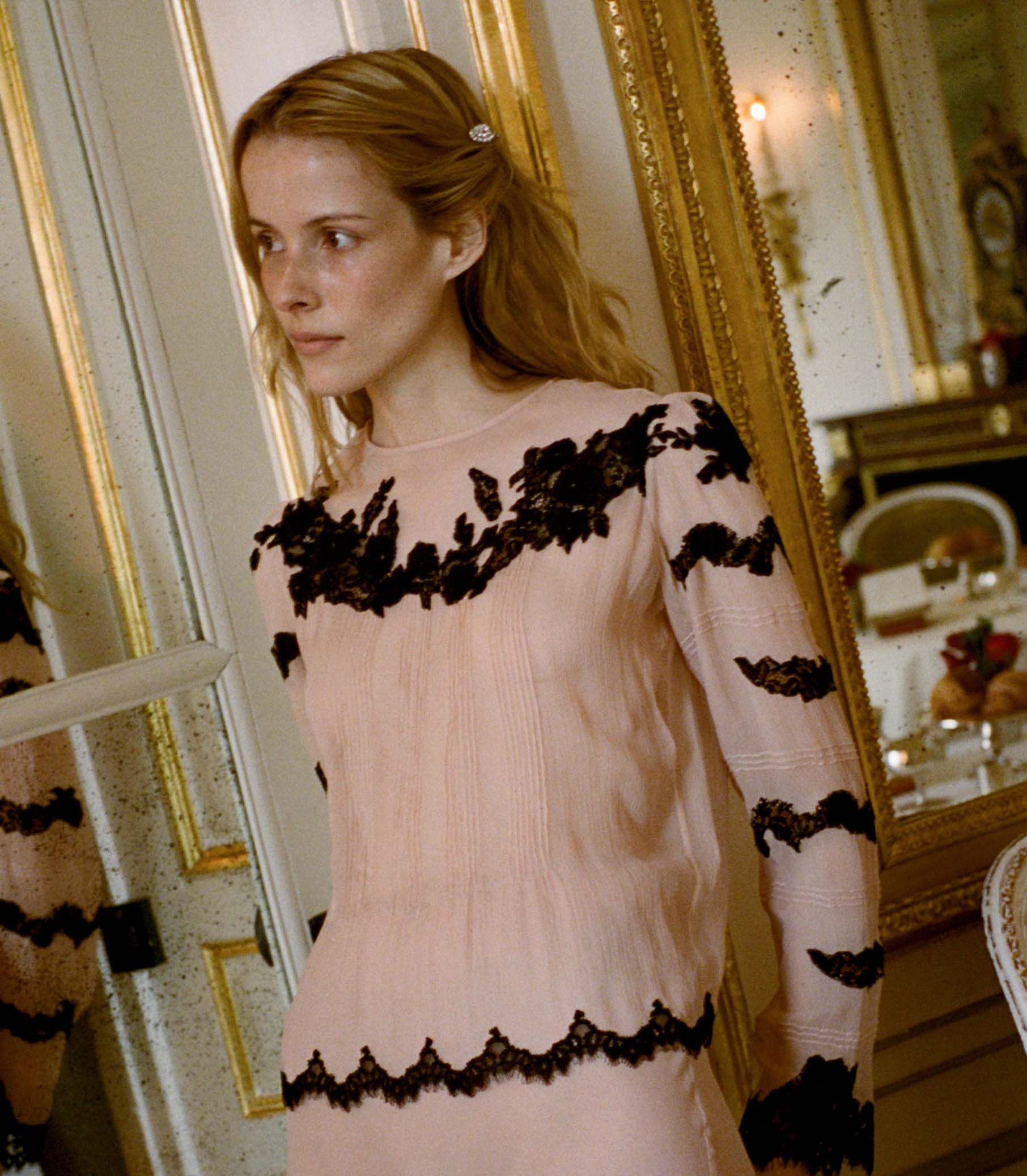 Woman wearing a pink blouse with black lace details in an elegant room. 1
