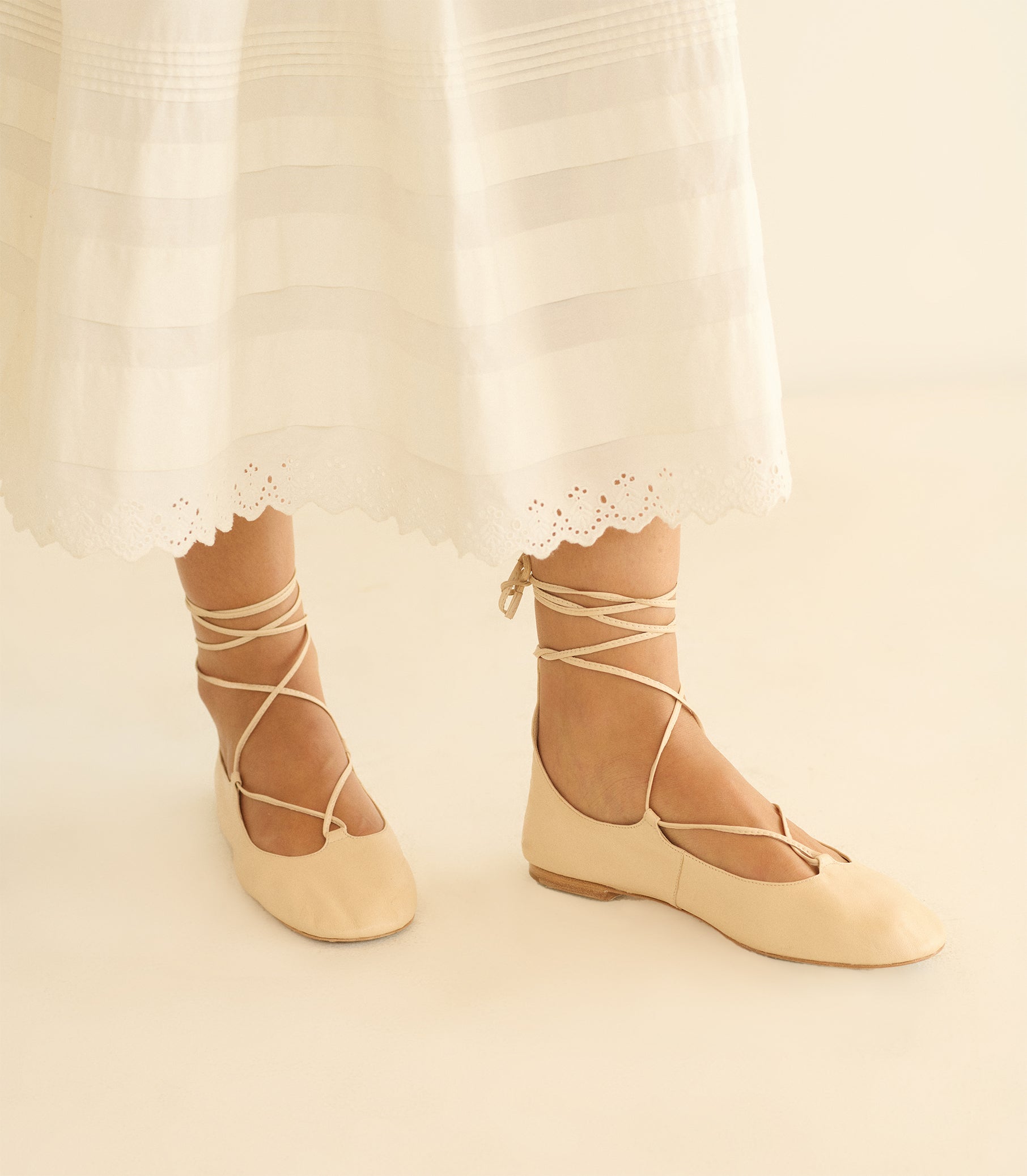 Beige ballet flats with lace-up design worn with a white dress.