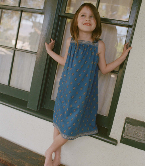 Young girl in a blue paisley dress standing by a window