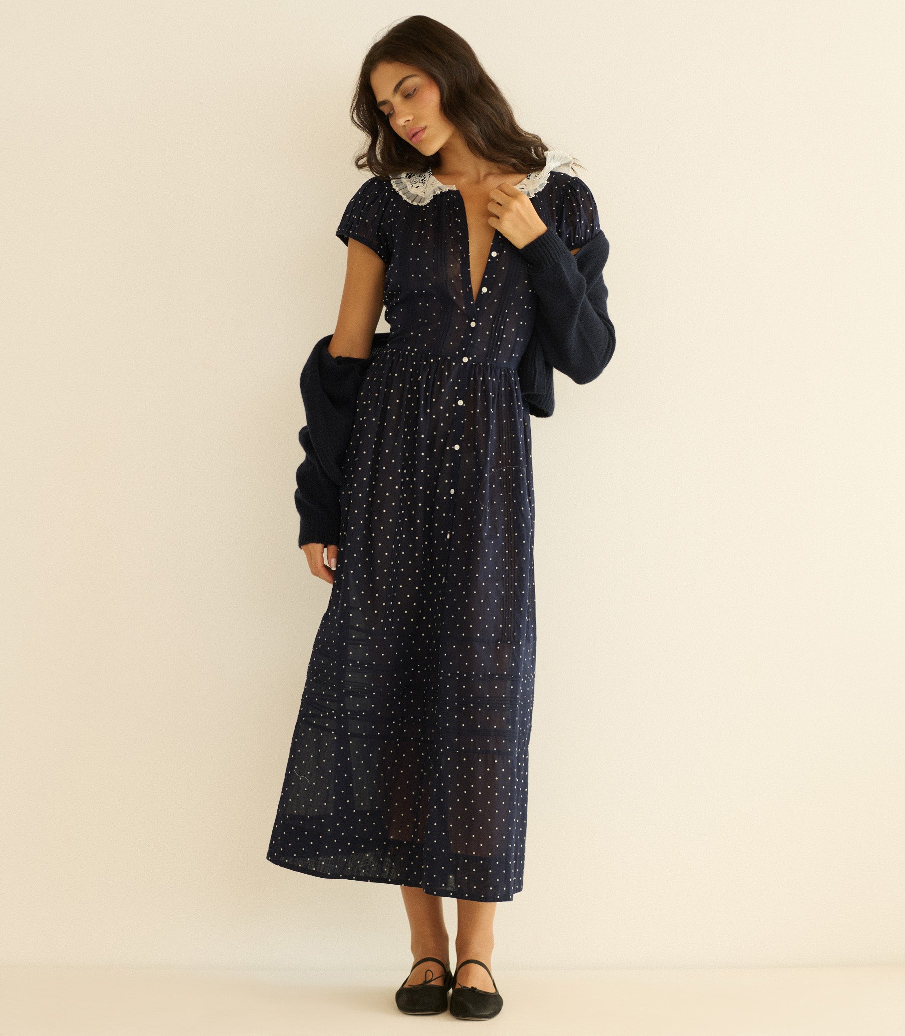 Woman wearing a dark blue dress with white polka dots and matching cardigan on a beige background