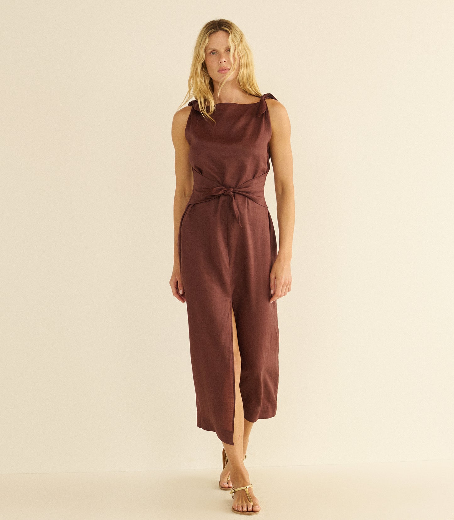 Woman wearing a mahogany dress with a slit on a beige background