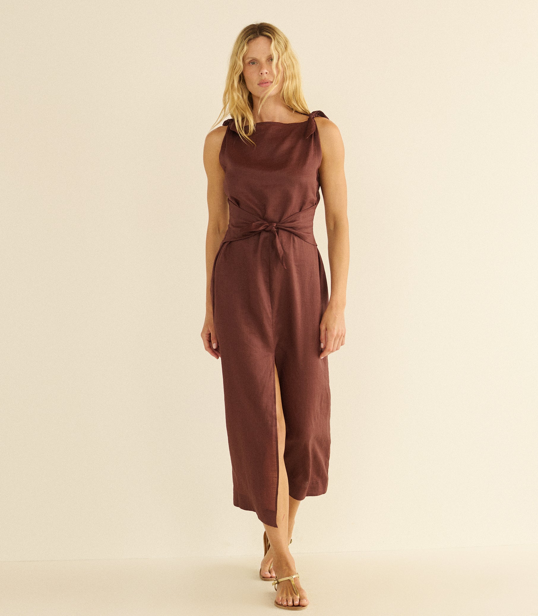 Woman wearing a mahogany dress with a slit on a beige background