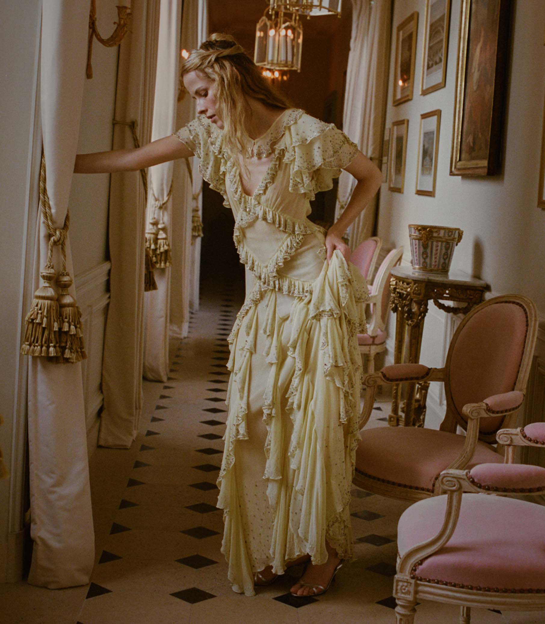 Woman in a vintage-style yellow dress standing in an elegant room with ornate decor. 1
