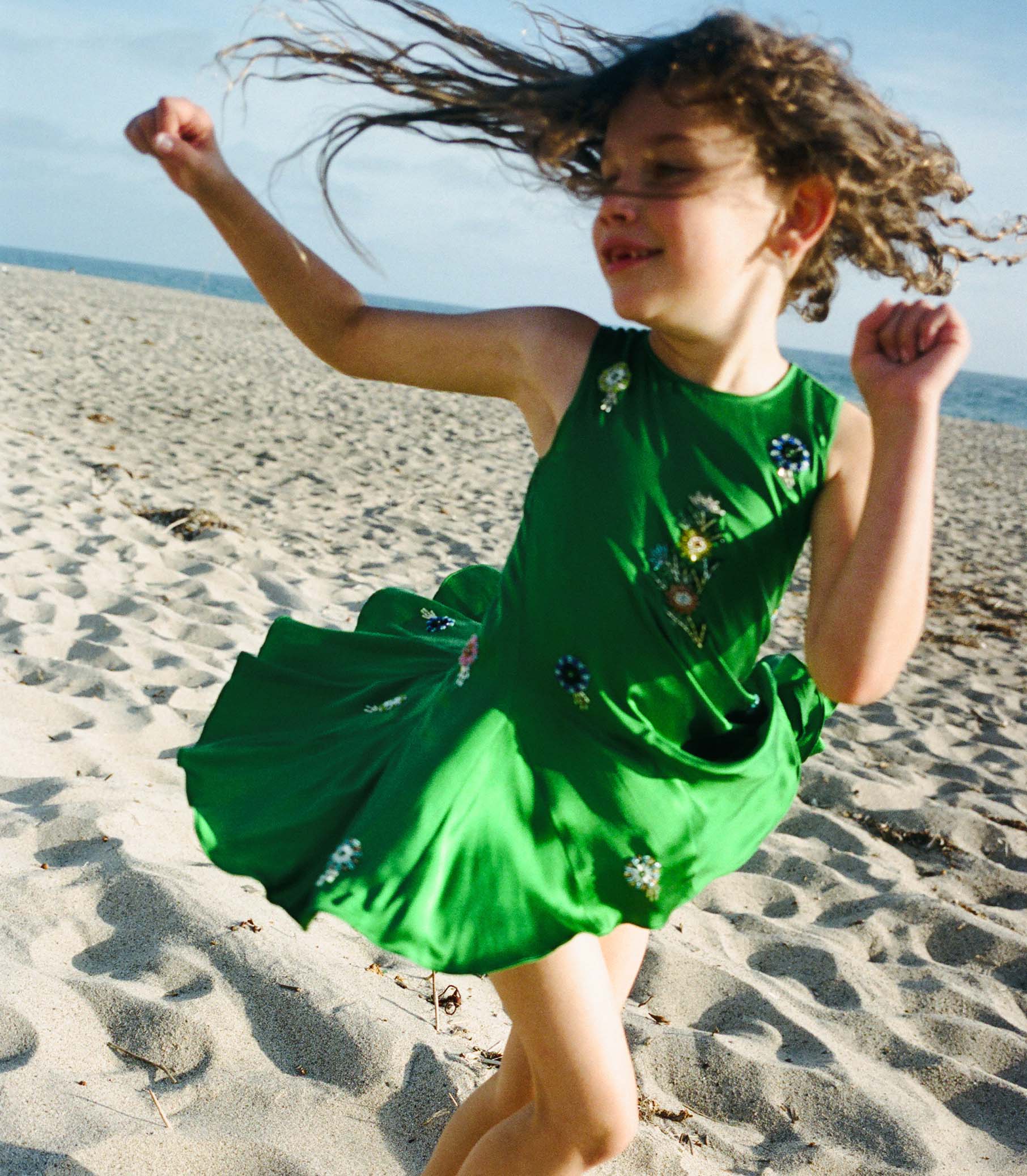Child in a green dress running on a sandy beach
