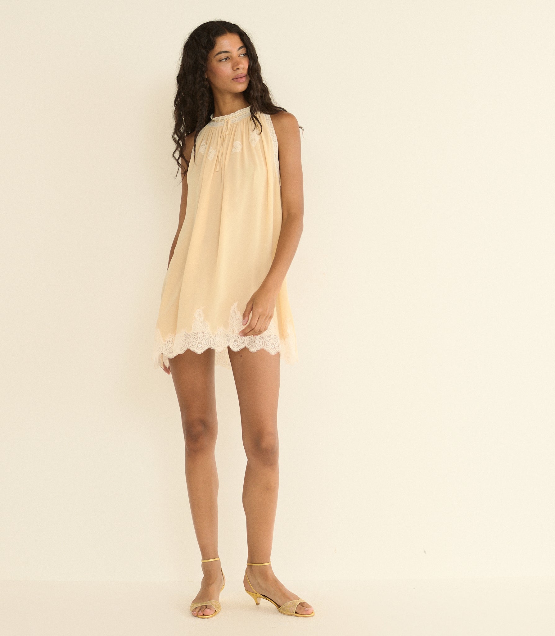 Woman wearing a light beige dress with lace trim on a plain background 1
