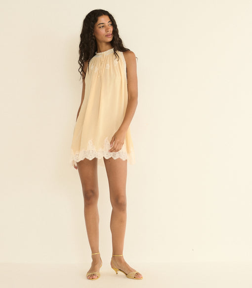 Woman wearing a light beige dress with lace trim on a plain background