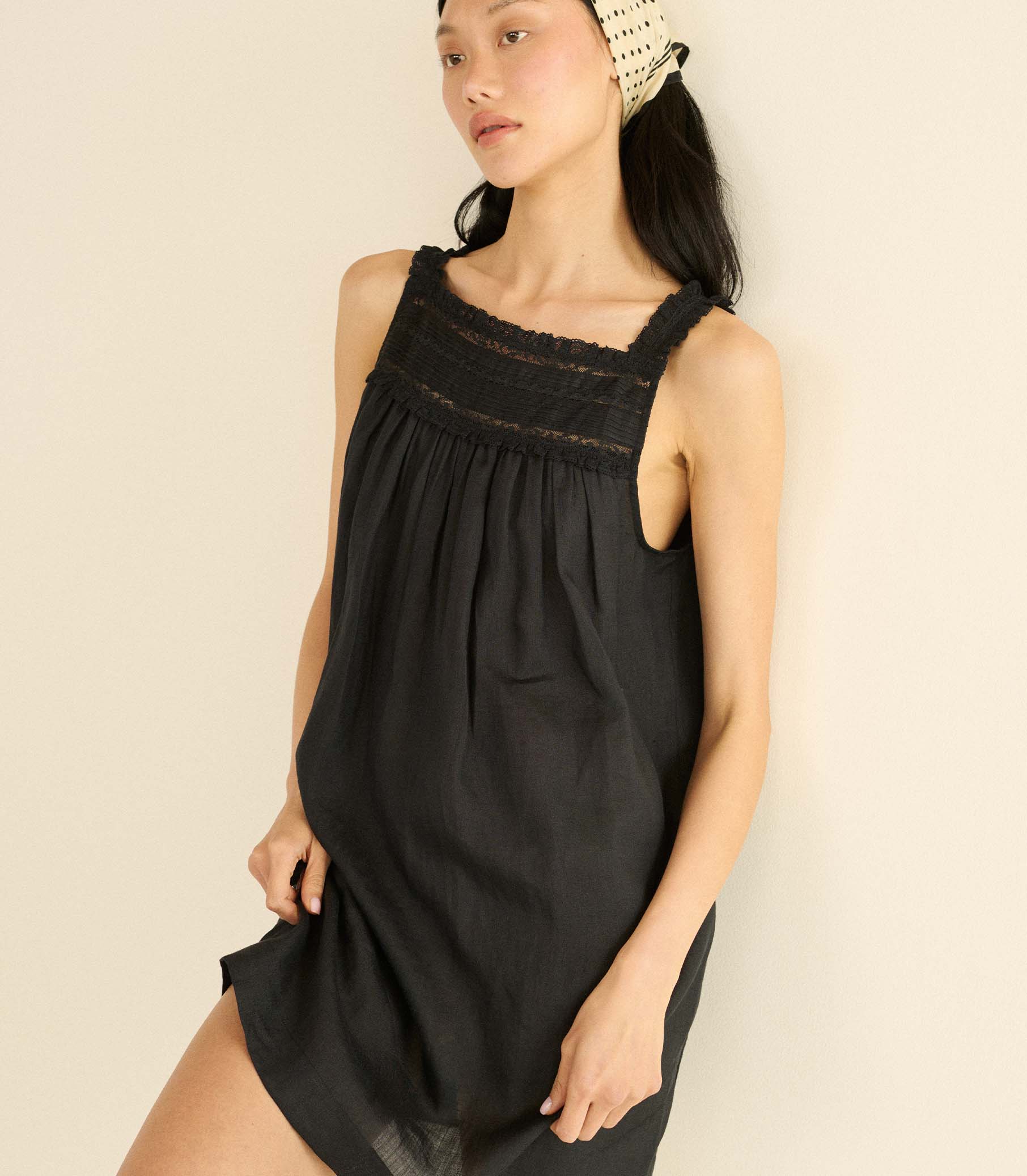 Woman wearing a black sleeveless mini dress with lace details on a beige background 1
