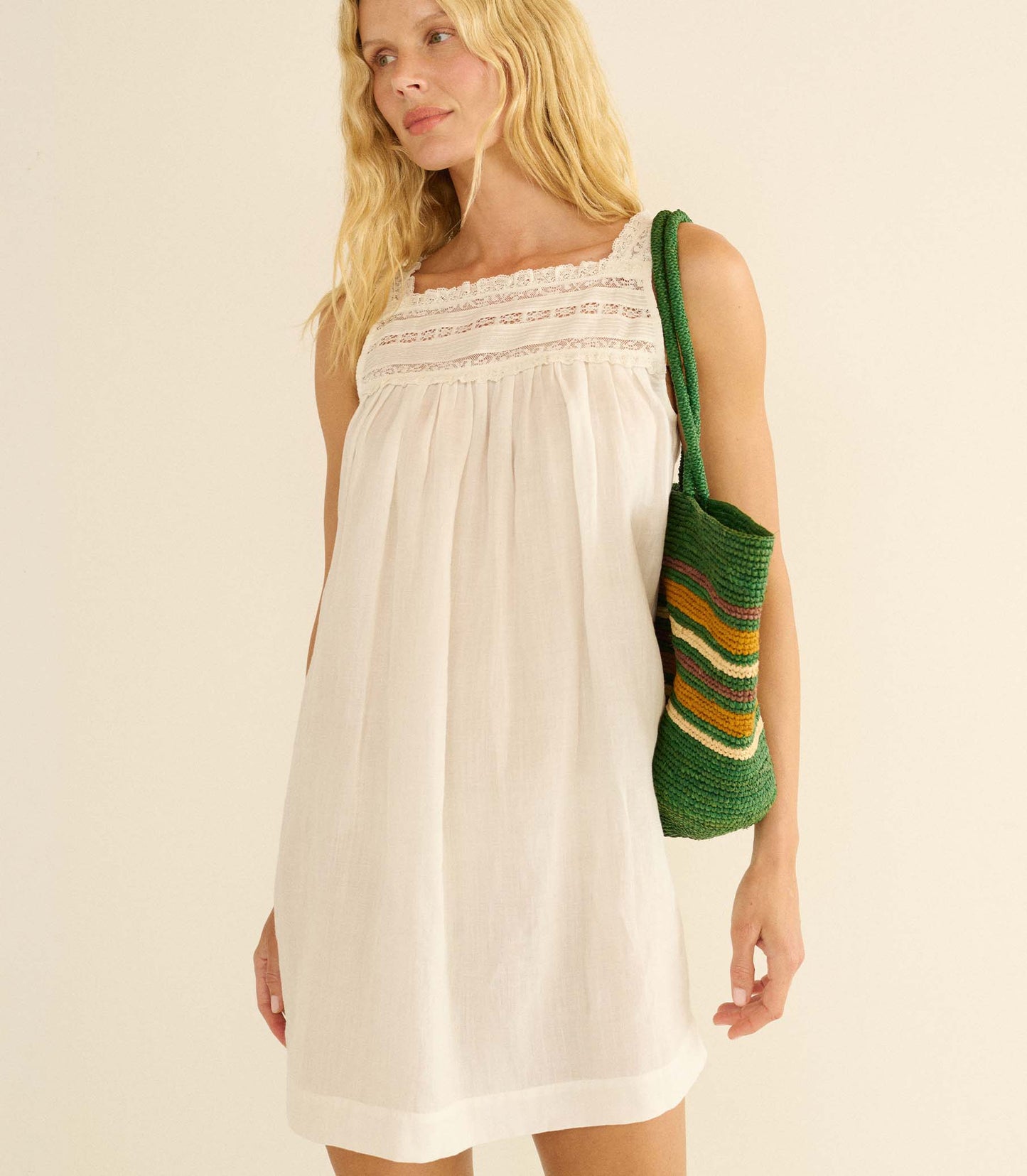 Woman wearing a white dress holding a green and brown striped bag against a beige background