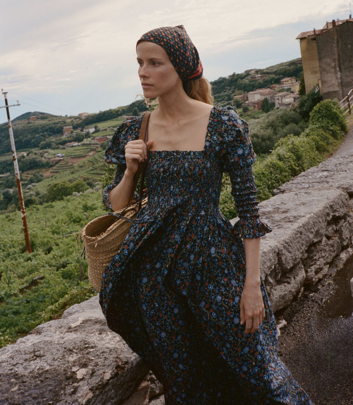 Woman in a floral dress standing on a stone wall with a scenic background