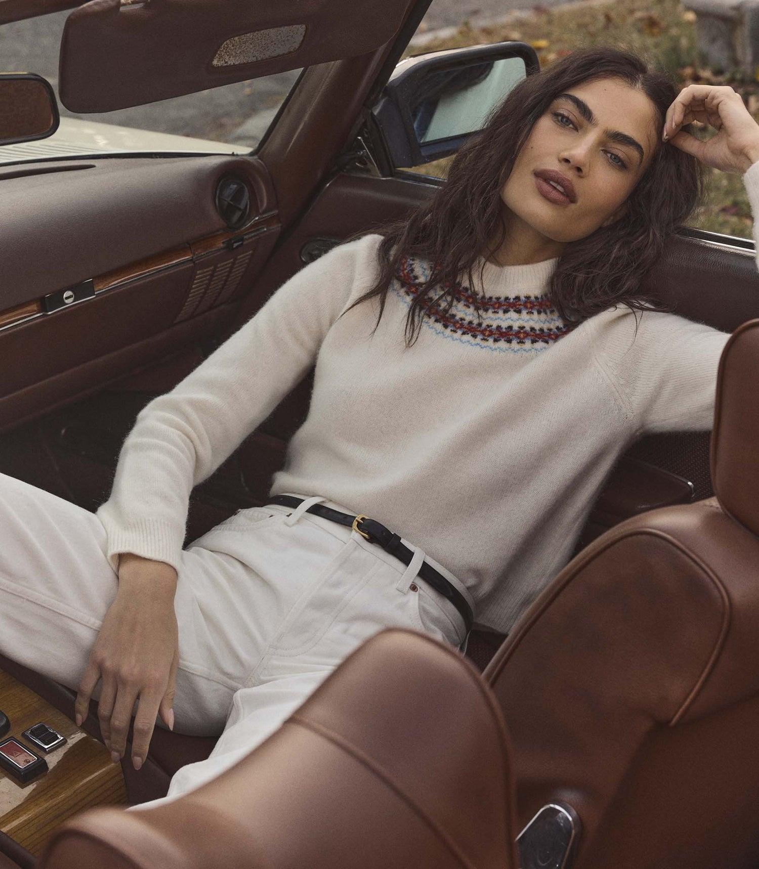 Woman wearing a cream fair isle sweater, sitting inside a vintage car with a brown interior