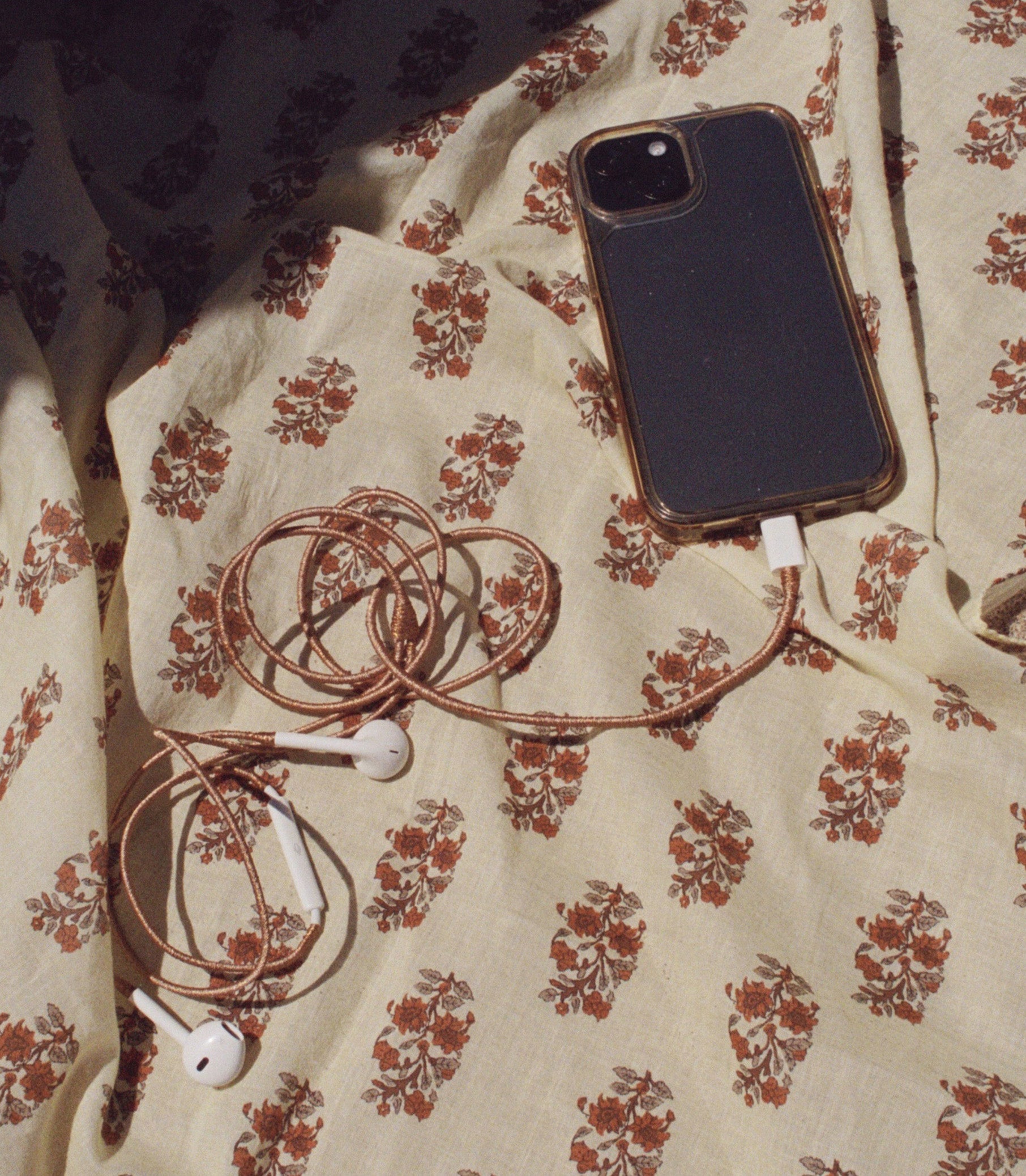 Cellphone with copper earphones on a floral blanket 1
