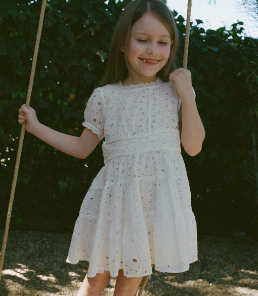 Young girl in a white dress on a swing with greenery in the background