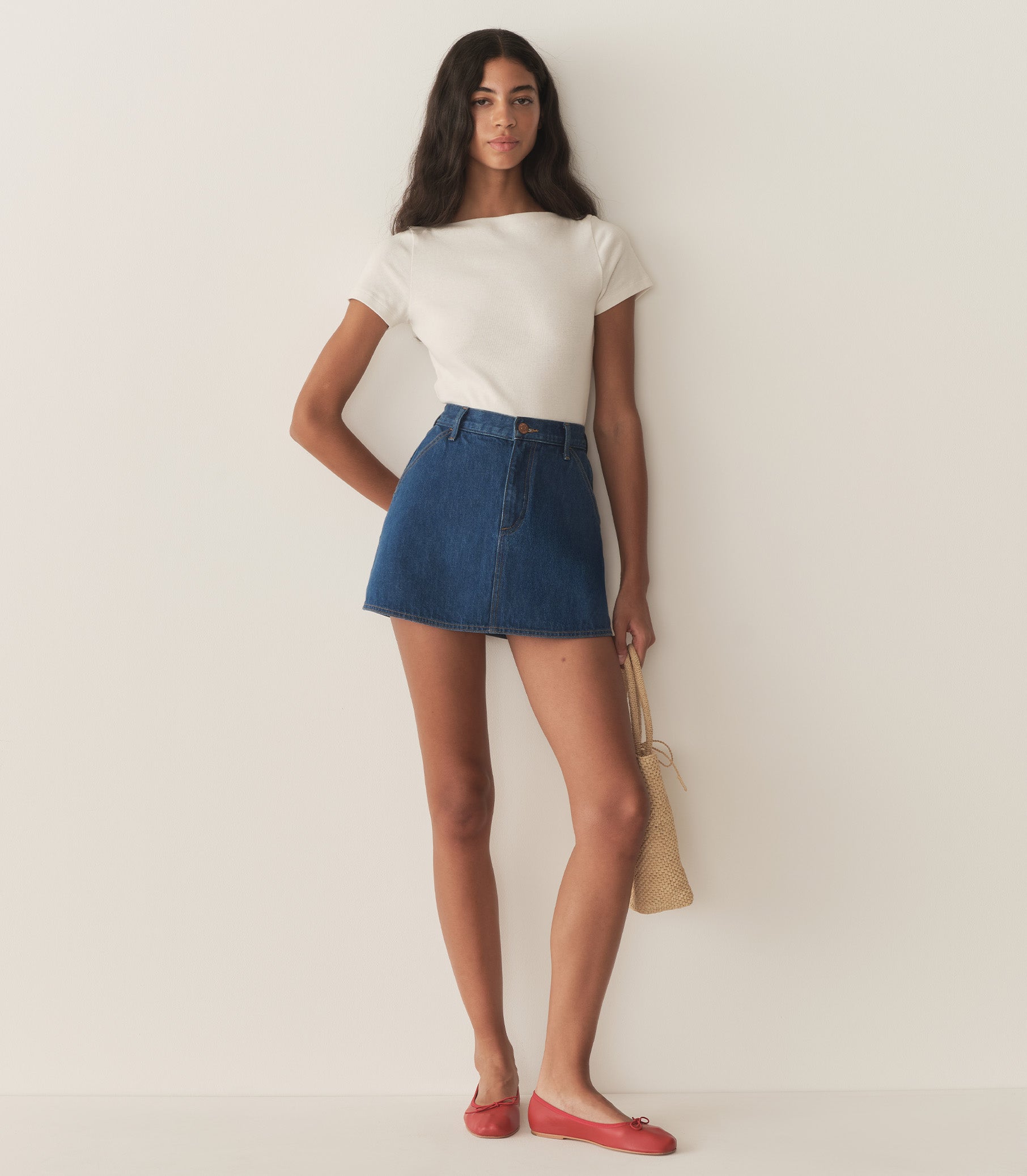 Rocio is wearing a denim A-Line skirt paired with a white top and red flats.