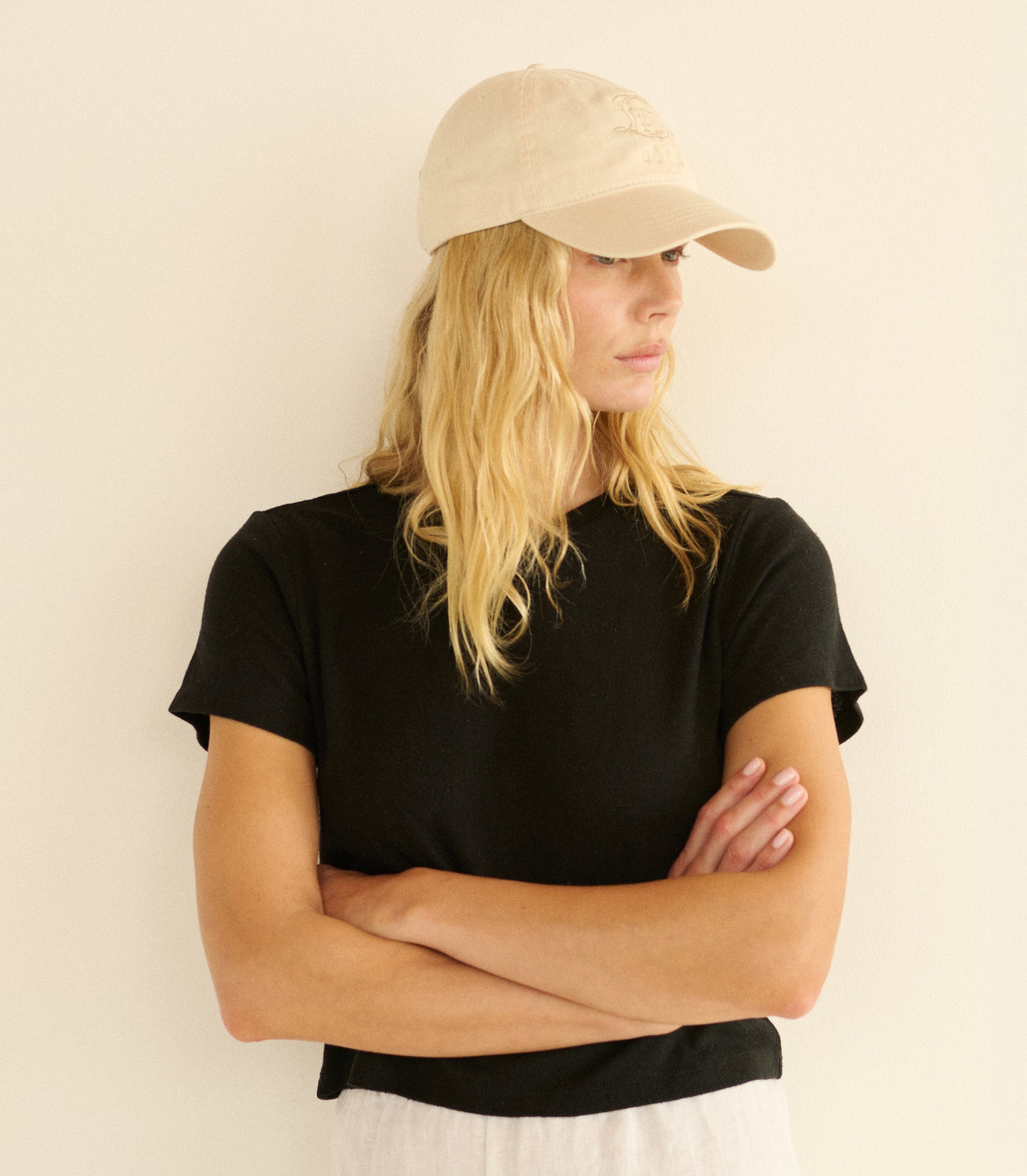 Woman wearing a black t-shirt and beige cap against a plain background 1
