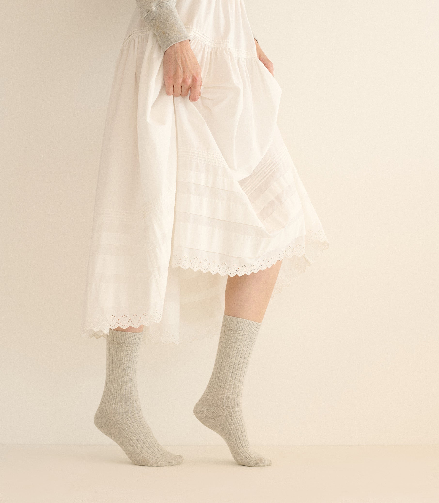 Person wearing a white dress with lace details and gray socks on a plain background