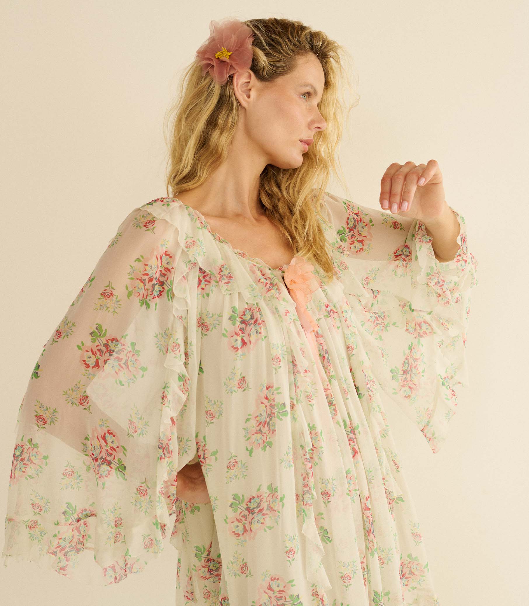 Woman wearing a white floral dress and pink floral barrette with a plain background