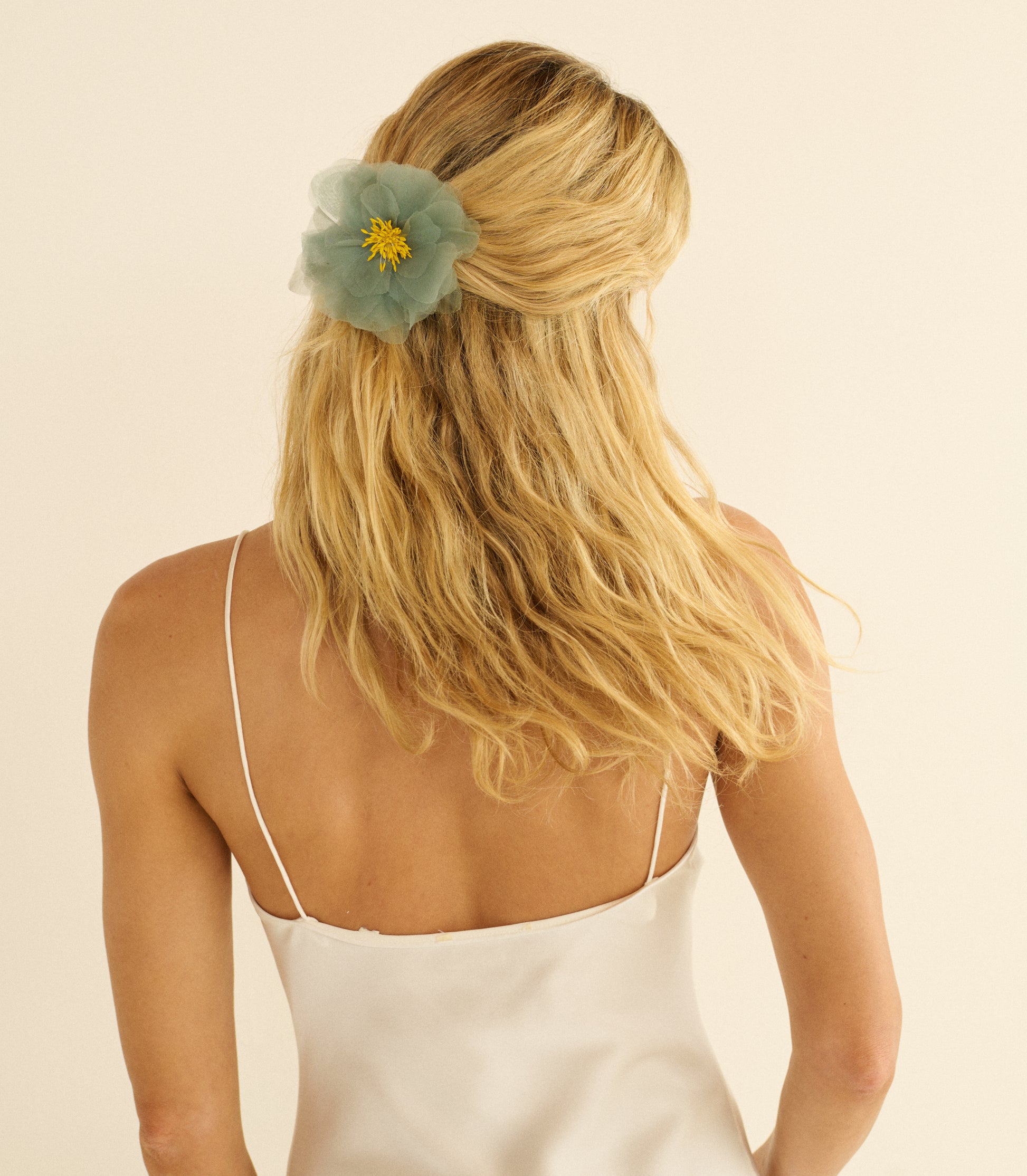 Woman with blonde hair wearing a teal floral hair accessory against a beige background 1

