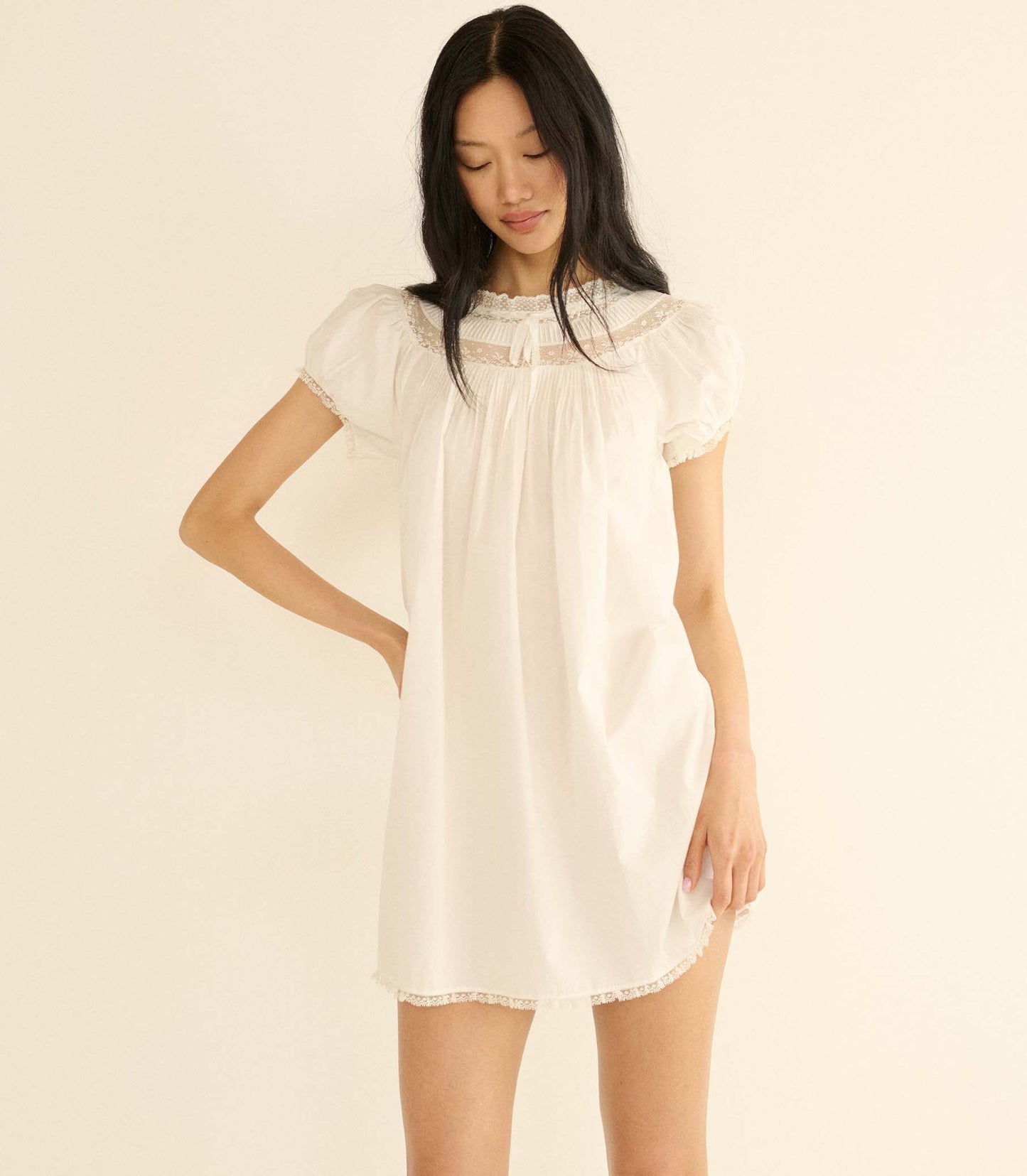 Woman wearing a white lace dress against a beige background
