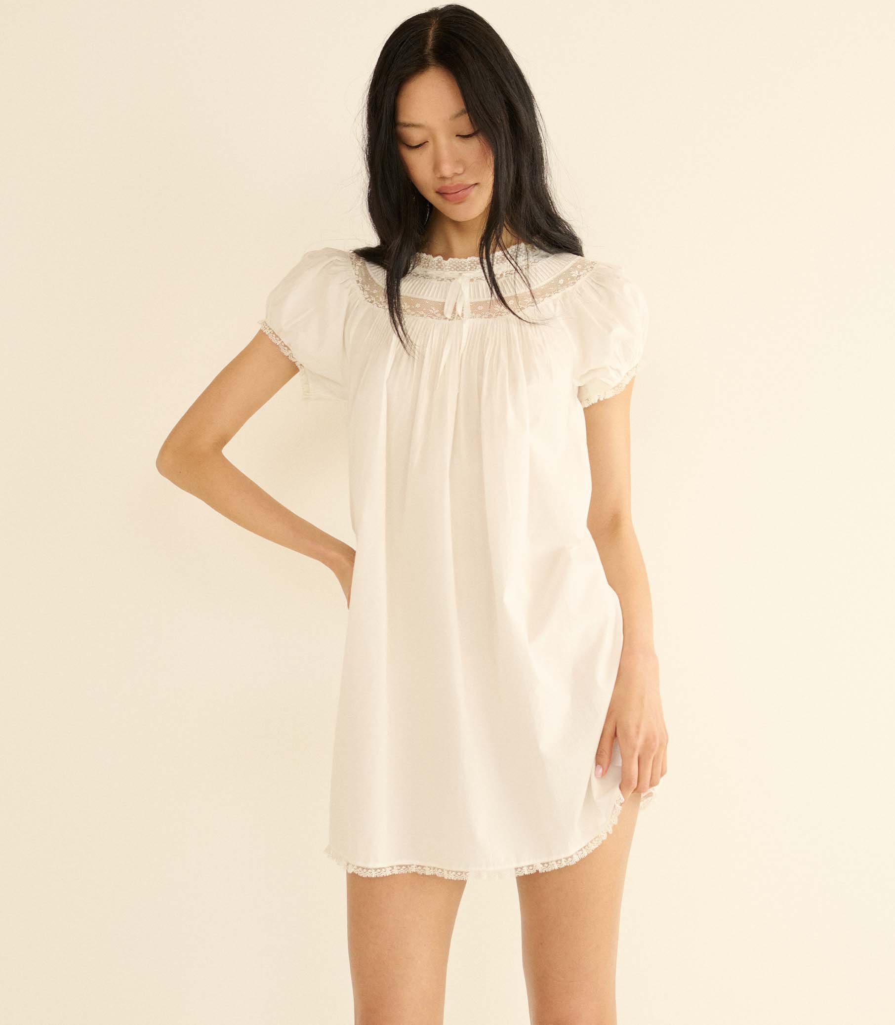 Woman wearing a white lace dress against a beige background 1
