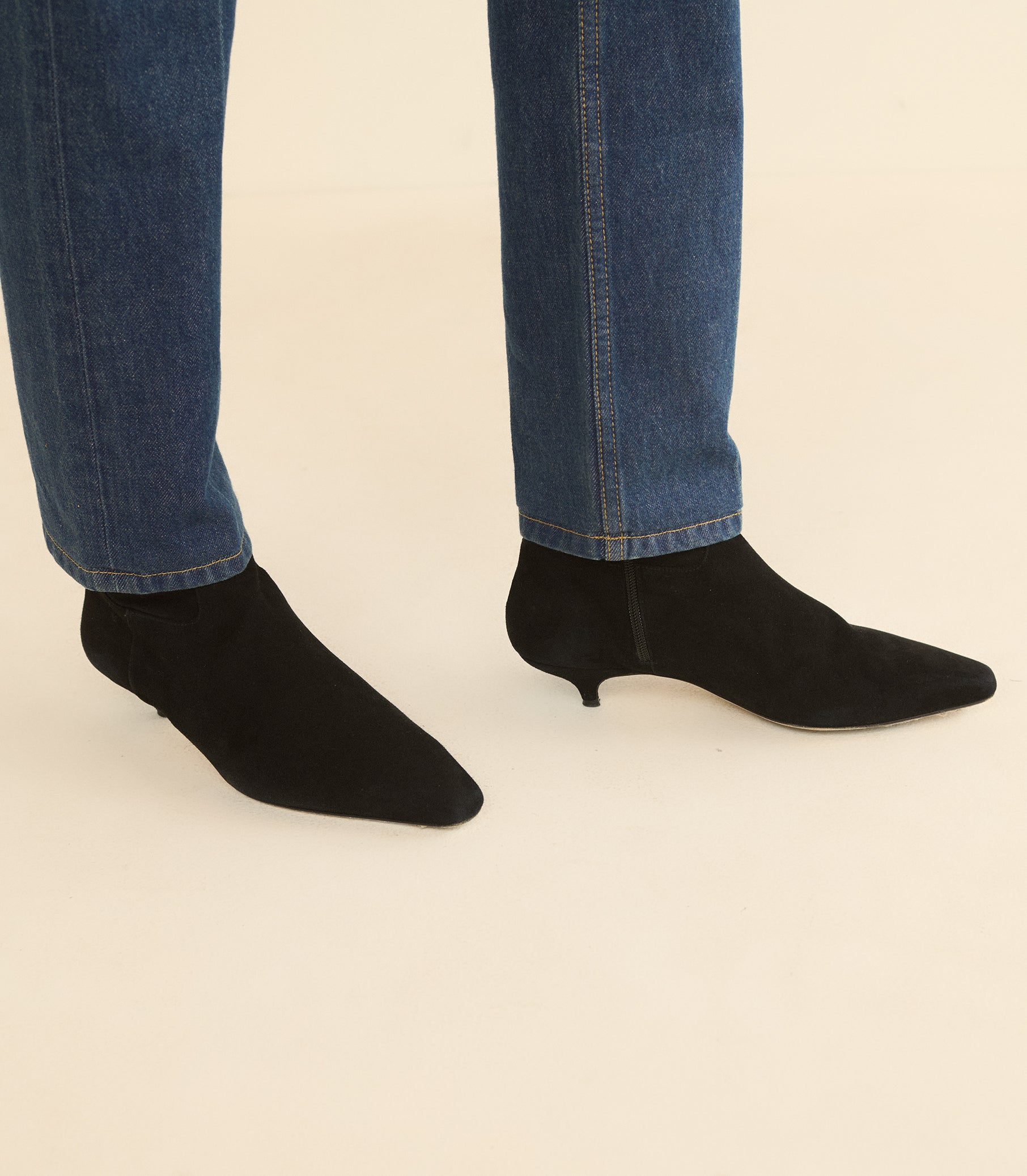 Black pointed-toe ankle boots with kitten heels, shown on a model wearing blue jeans against a plain beige background. 1
