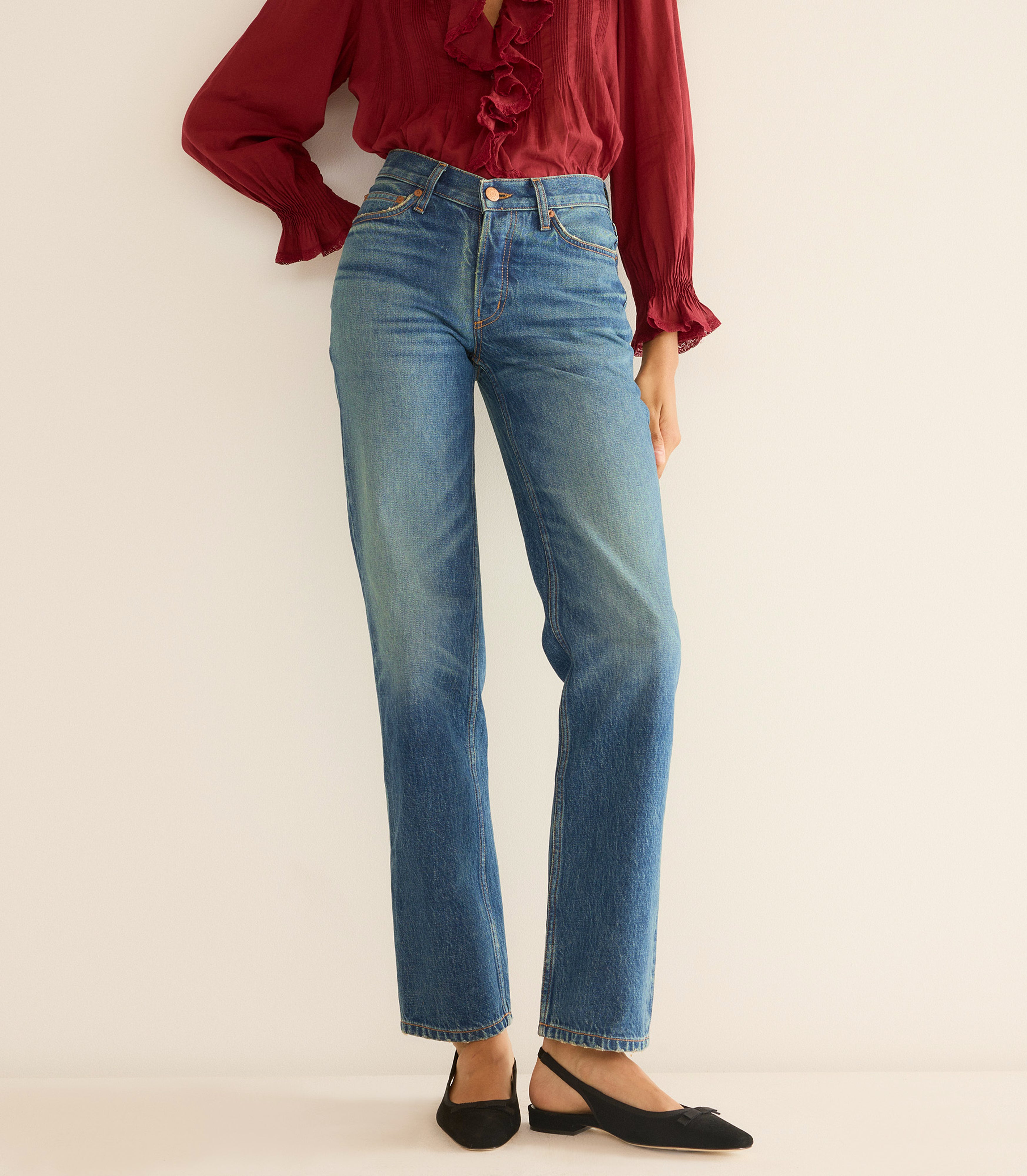 Person wearing blue jeans and a red blouse on a beige background