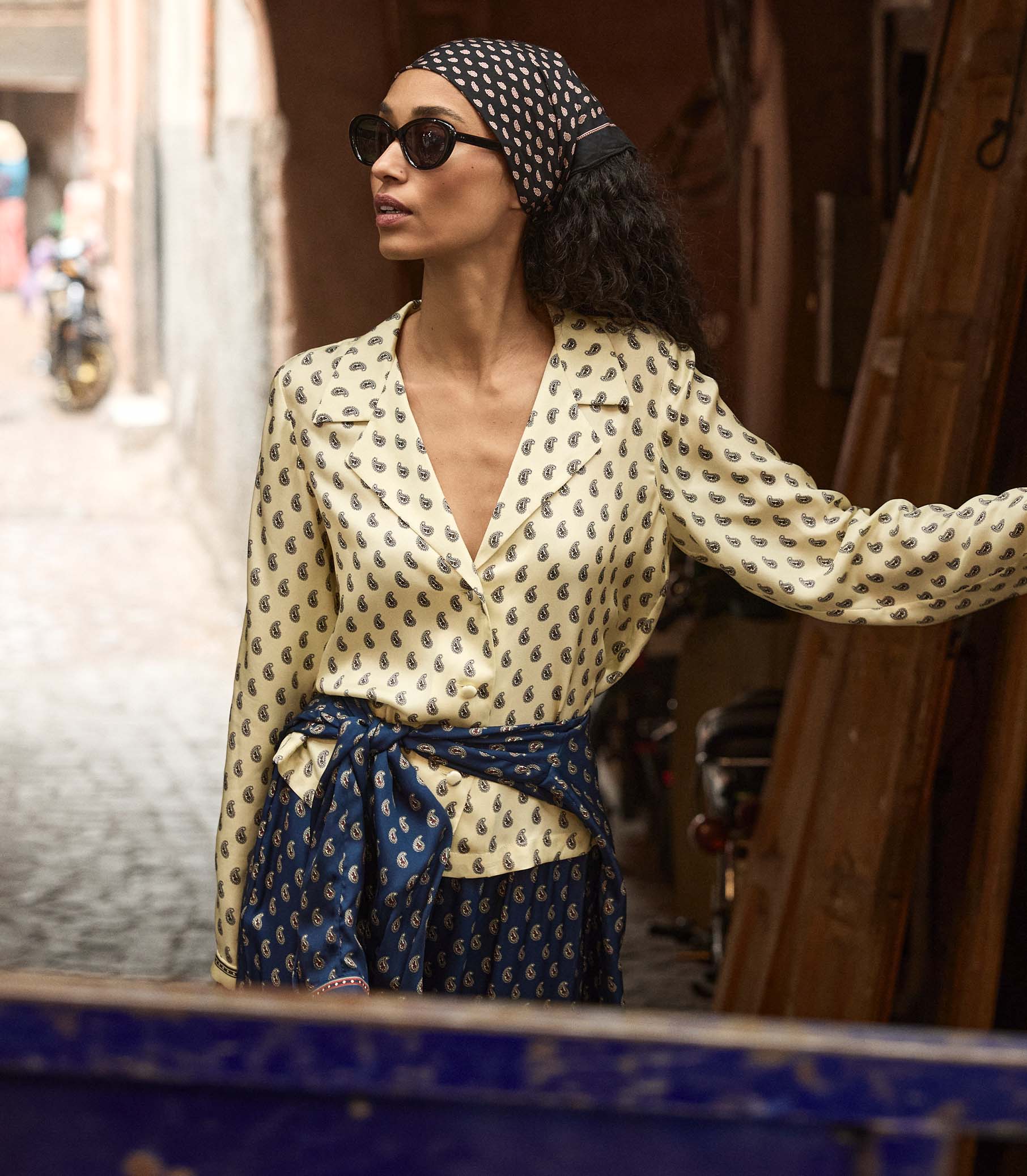 Woman wearing a yellow patterned blouse and headscarf in an urban setting 1

