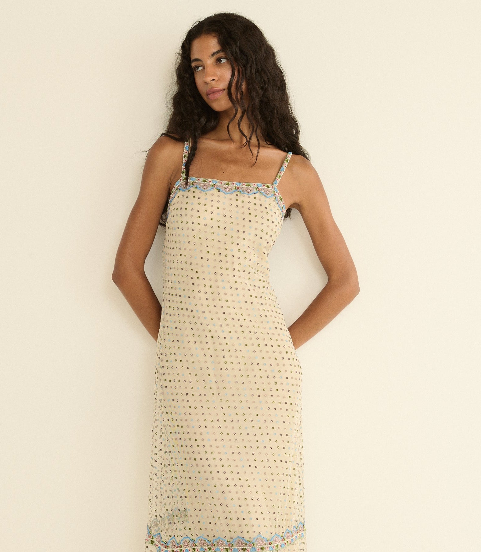 Woman wearing a beige patterned dress with blue trim against a plain background