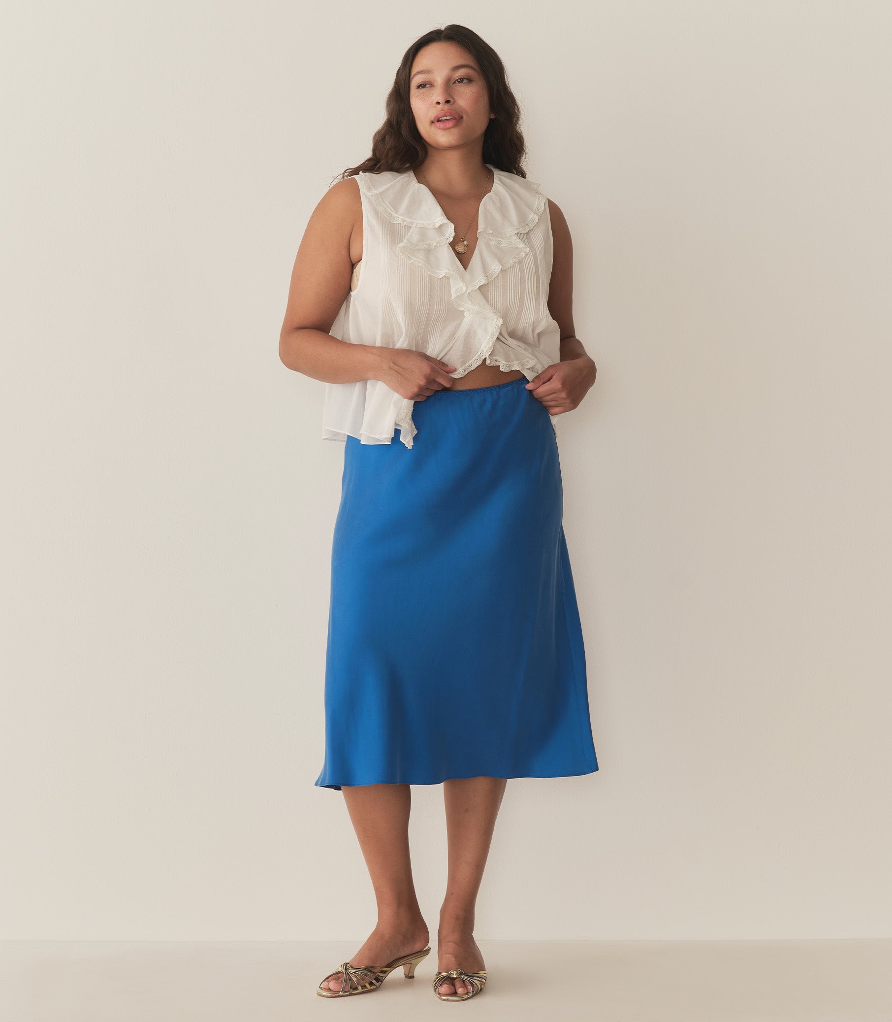 Alana is wearing a blue midi skirt paired with a white sleeveless top and metallic kitten heels. 1
