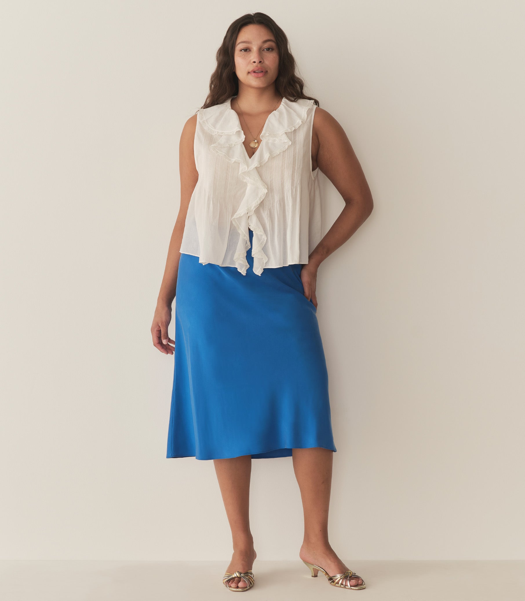 Alana is wearing a blue midi skirt paired with a white sleeveless top and metallic kitten heels. 2
