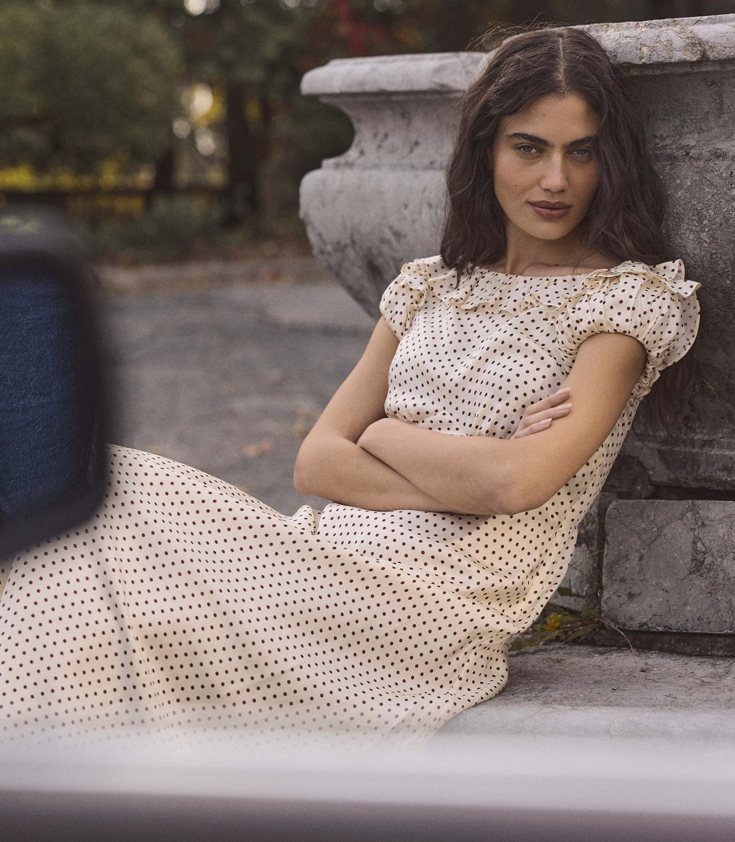 Woman in a polka dot dress sitting against a stone wall outdoors