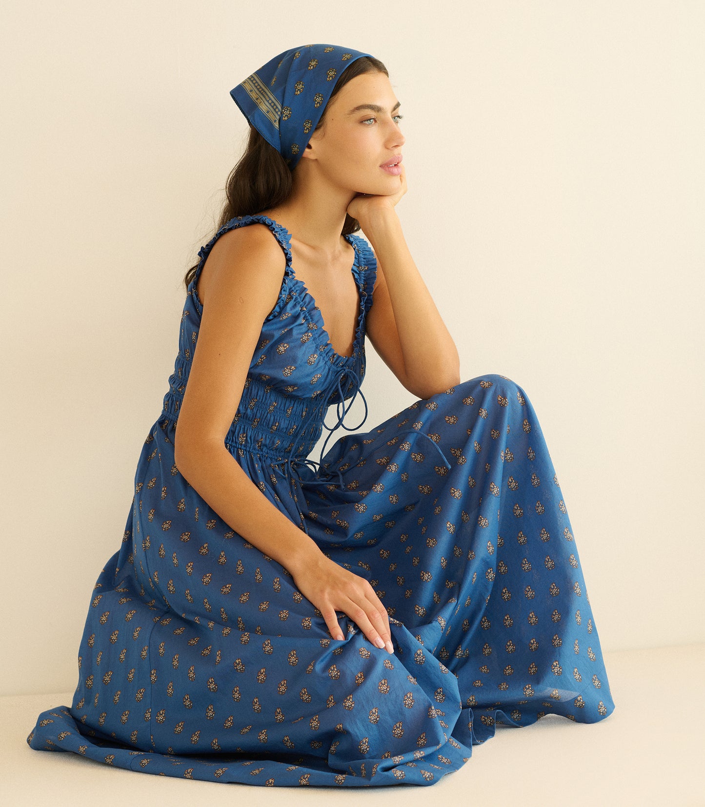 Woman wearing a blue paisley bandana with a matching dress on a beige background