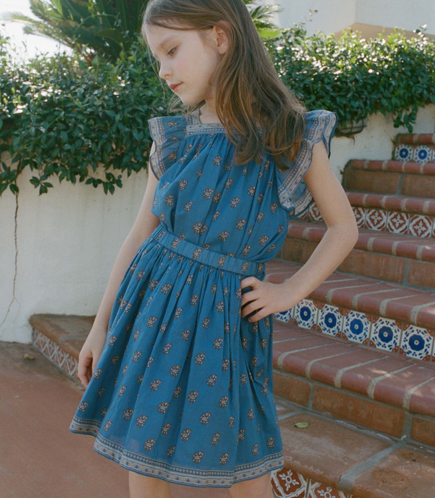 Young girl wearing a blue paisley skirt with a matching top outdoors. 1
