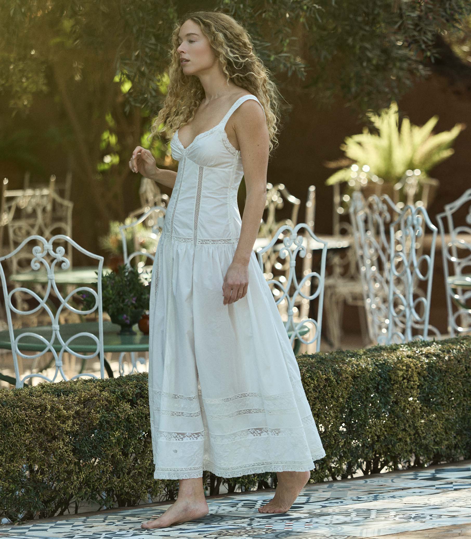 Woman in a white dress standing outdoors with garden furniture in the background 1
