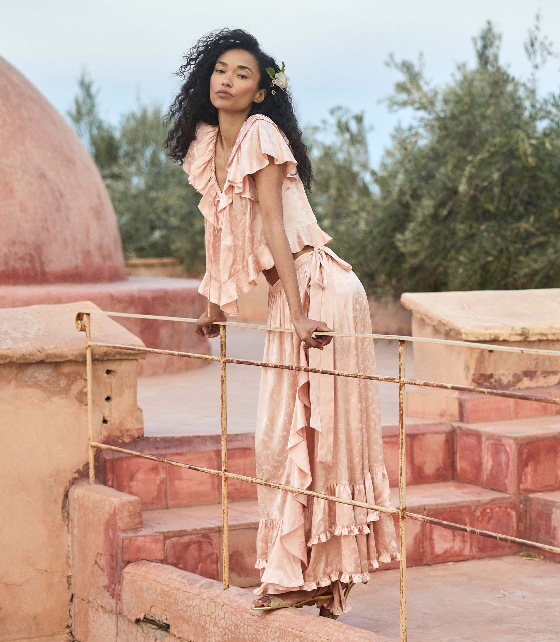 Woman in a flowing peach matching set standing on stone steps with greenery in the background 1
