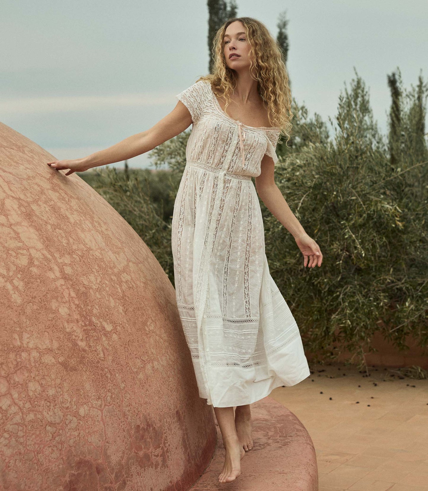 Woman in a white dress standing next to a large stone in a natural setting