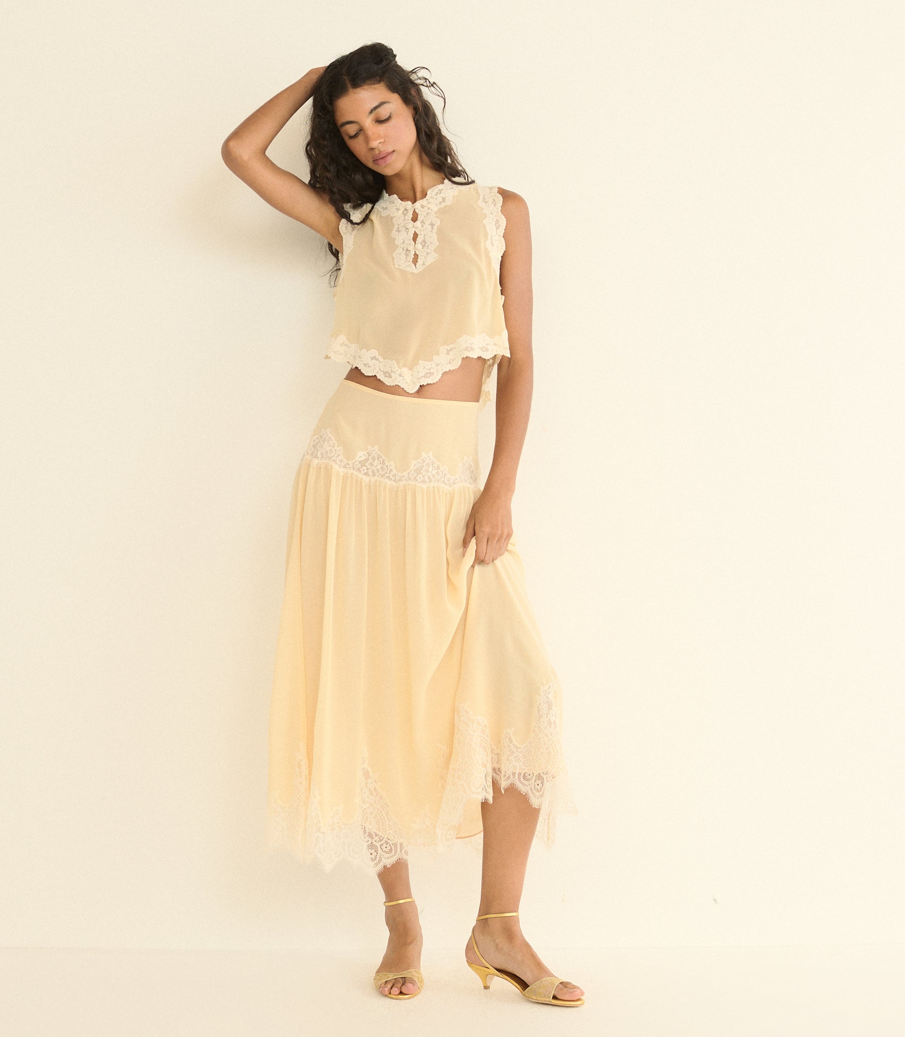 Woman wearing a light beige lace outfit against a plain background