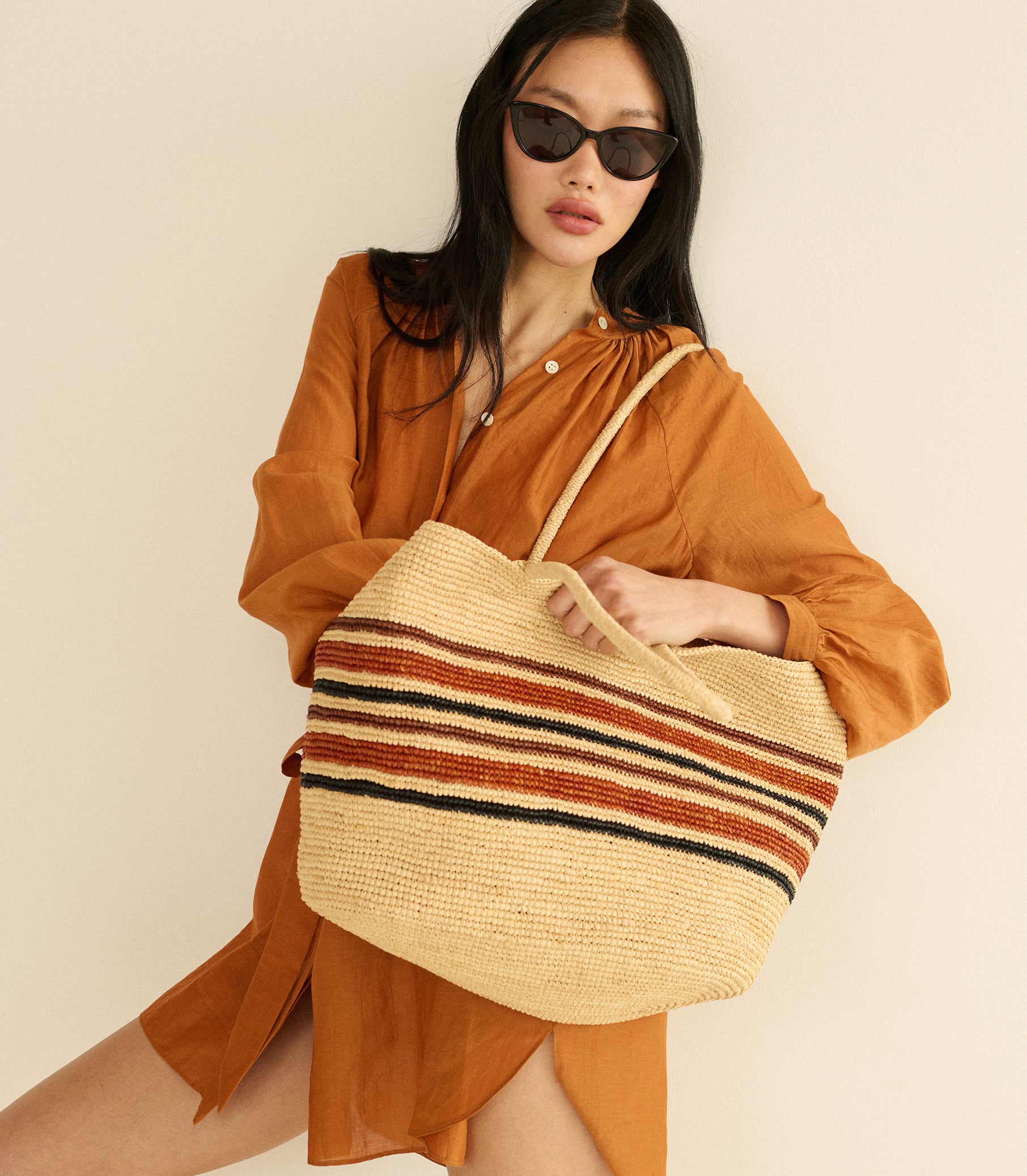 Woman holding a striped raffia bag against a beige background 1
