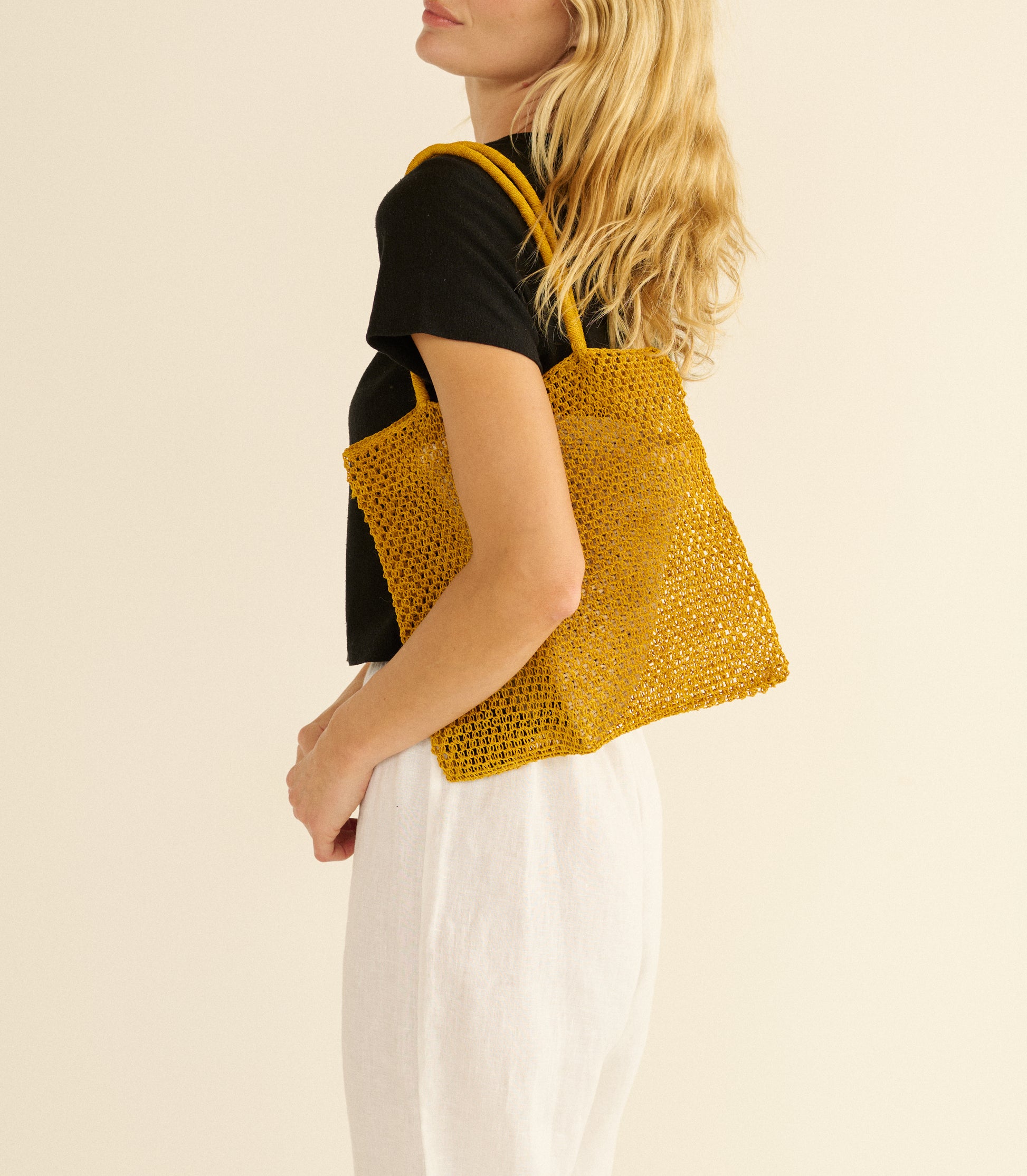 Woman holding a yellow knitted tote bag against a beige background 1
