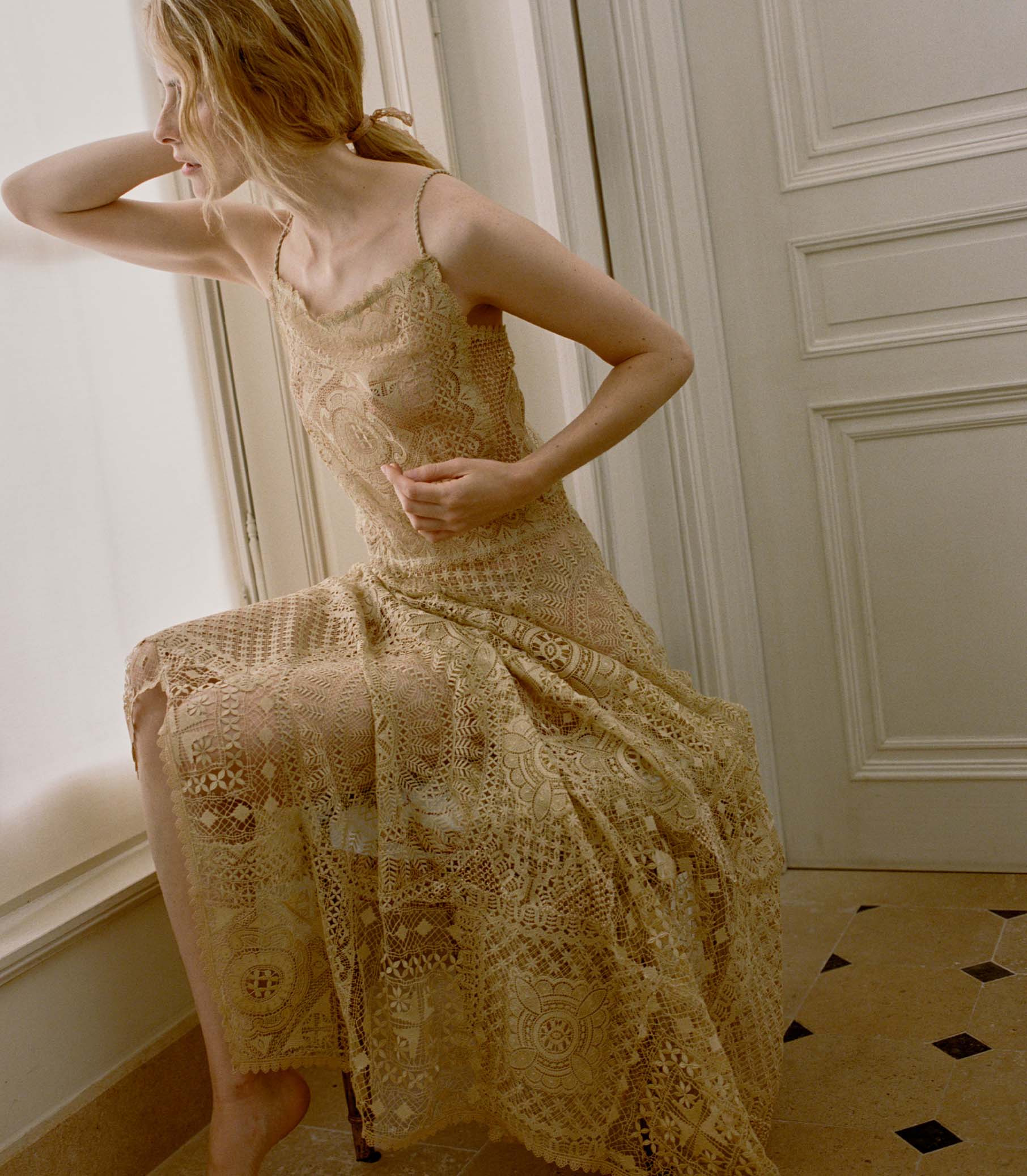 Woman wearing a pale gold crochet dress in an elegant room with white walls and a patterned floor. 1
