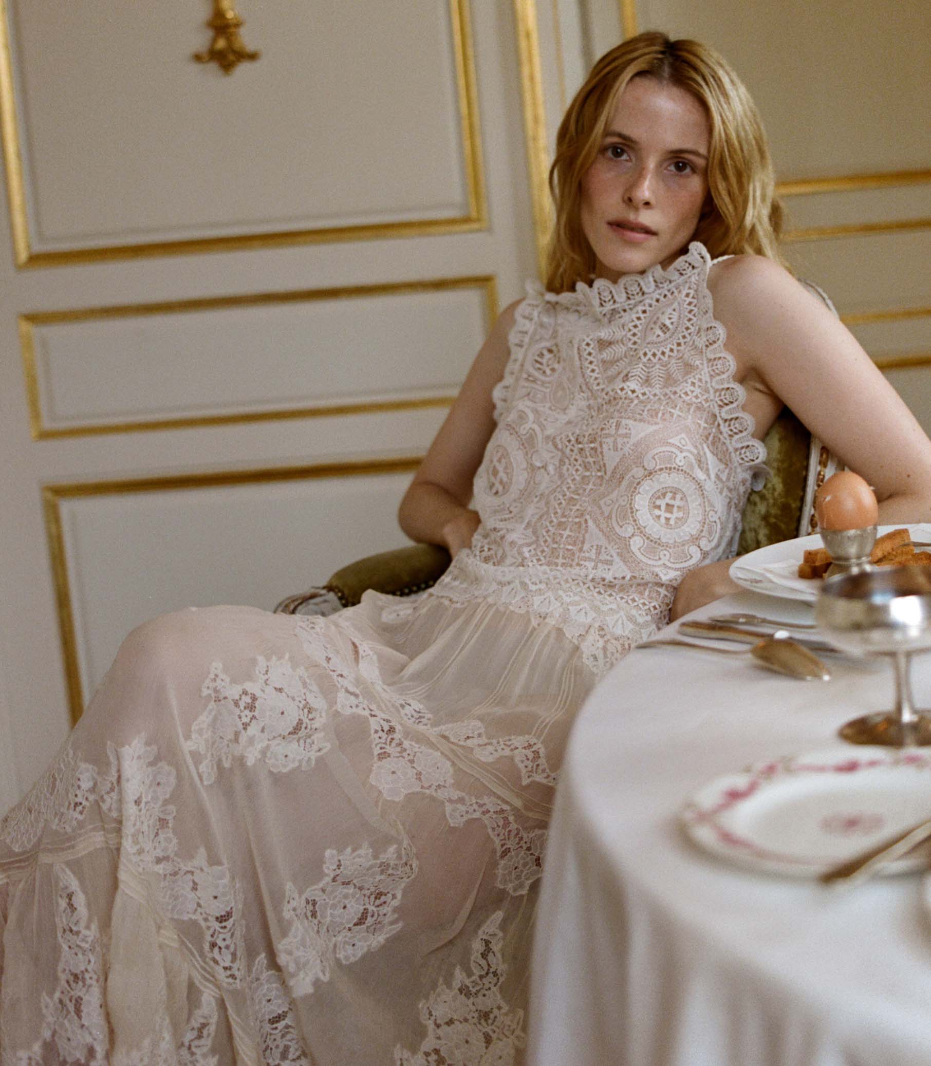 Woman wearing a white crochet lace top sitting at a table with a decorative setting. 1
