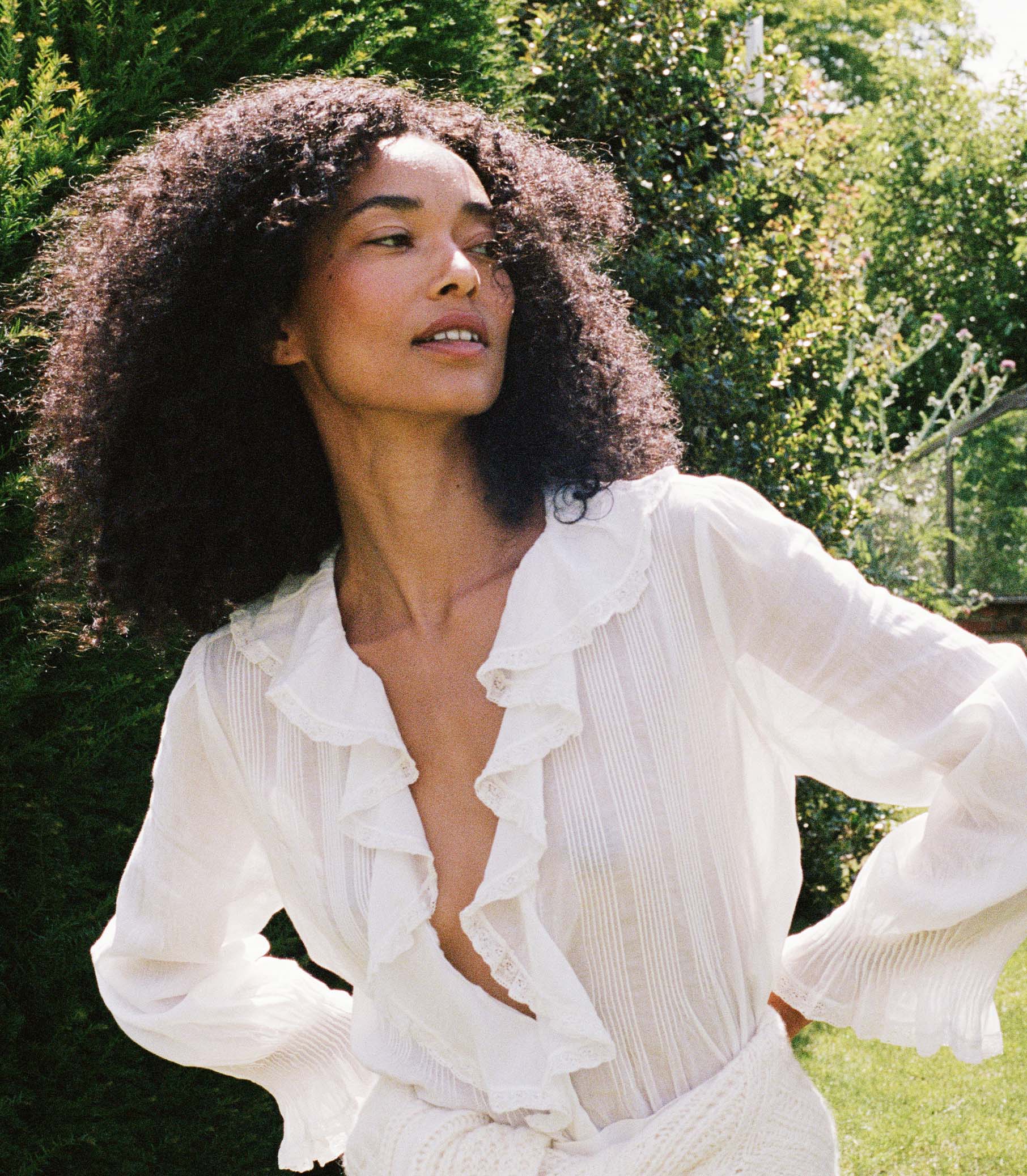Woman wearing a white blouse and white skirt amongst greenery 7
