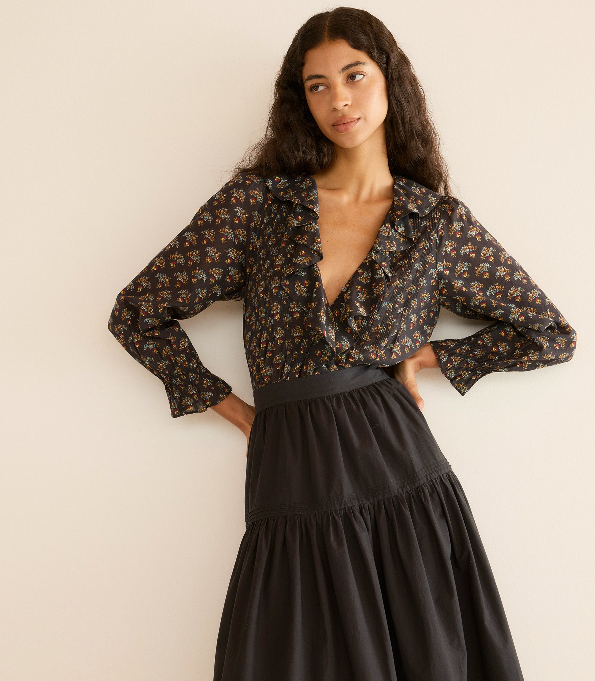Woman wearing a floral blouse and black skirt against a beige wall 1
