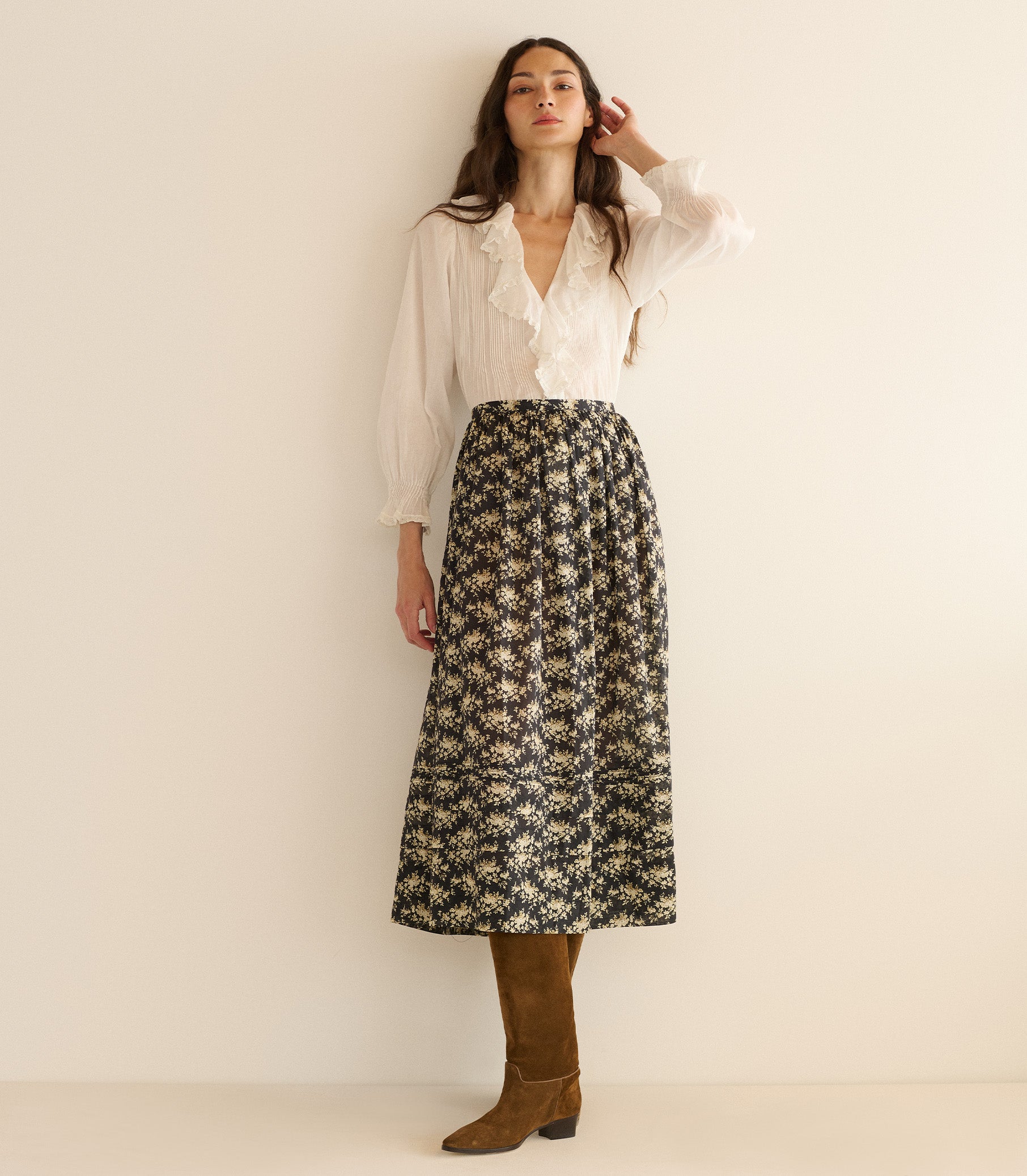Woman wearing a white blouse and floral skirt against a plain background 4
