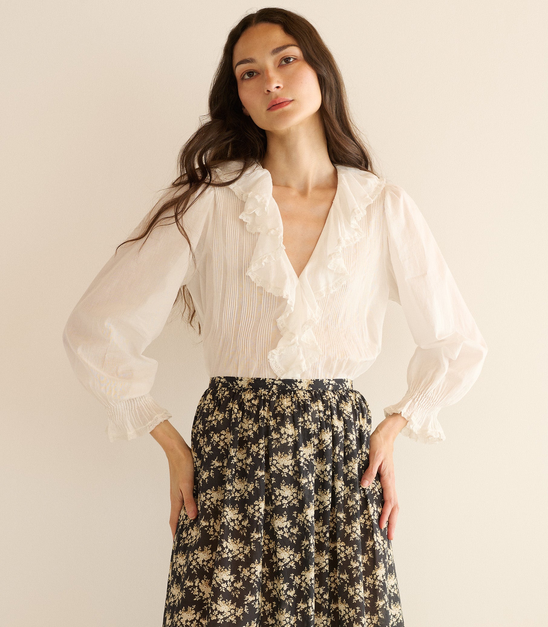 Woman wearing a white blouse and floral skirt against a plain background 3

