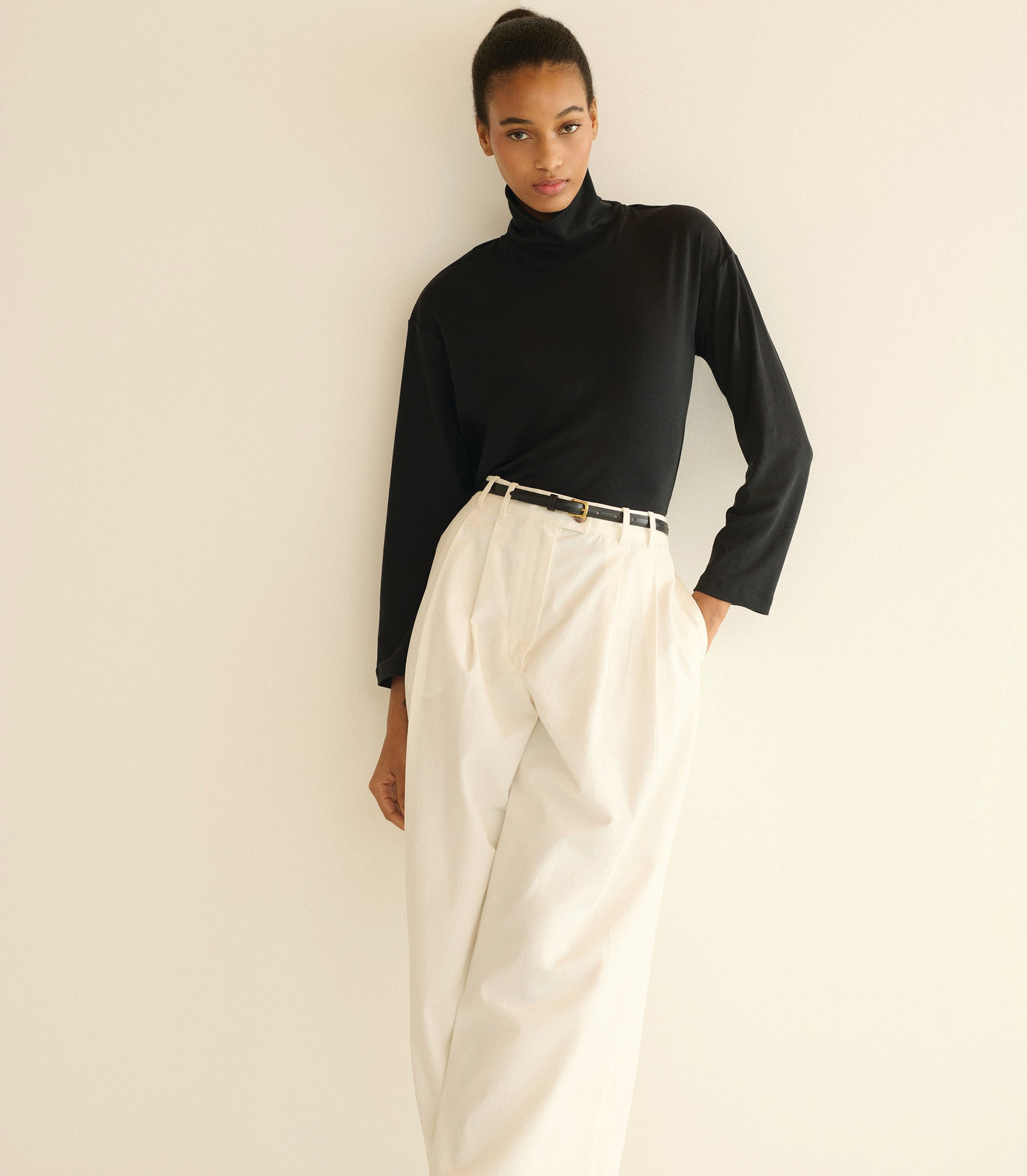 Person wearing a black turtleneck and white pants against a plain background 1

