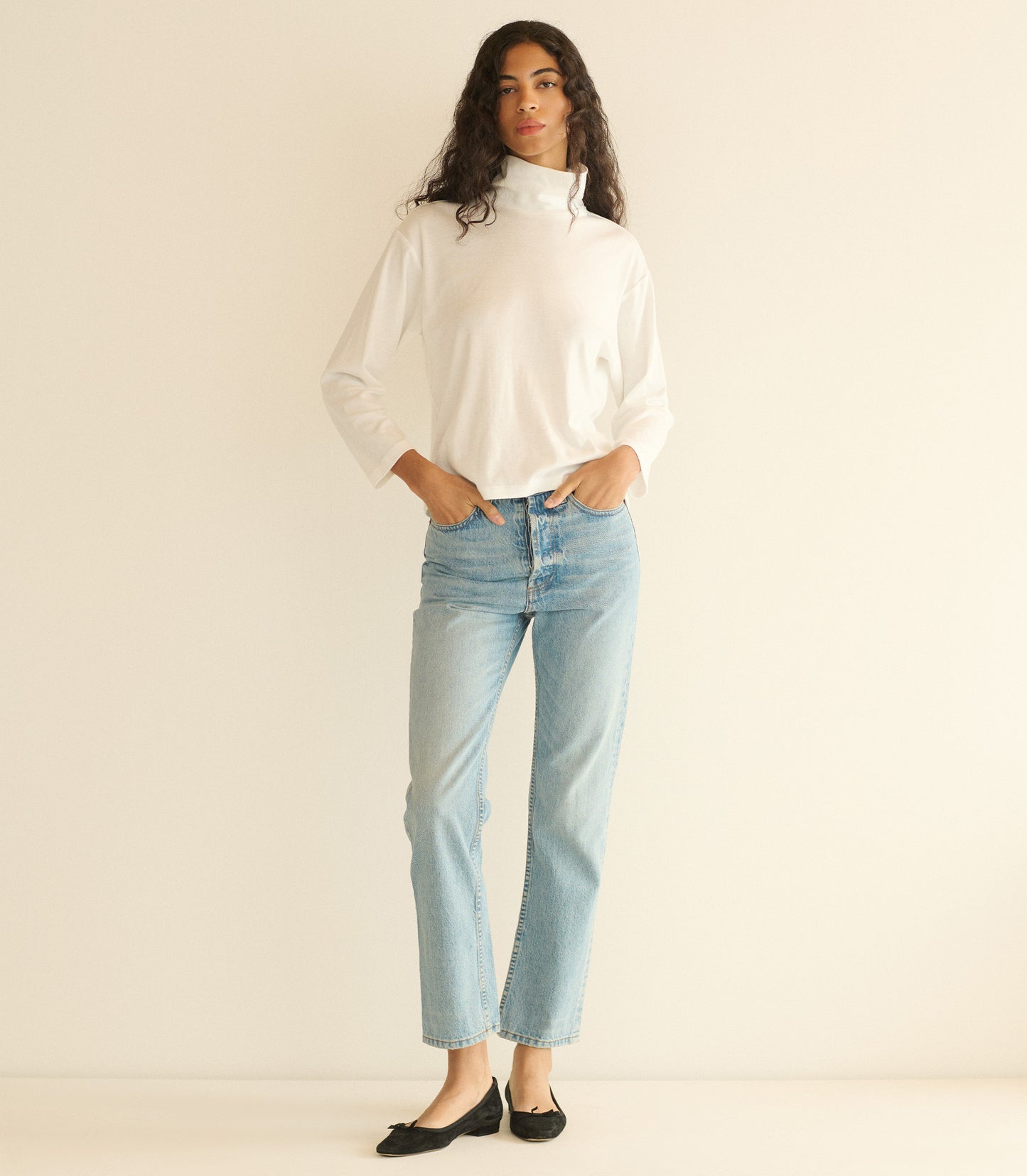 Woman wearing a white turtleneck sweater and light blue jeans on a beige background