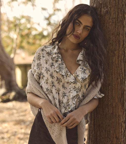 Woman in a floral blouse leaning against a tree in a natural setting
